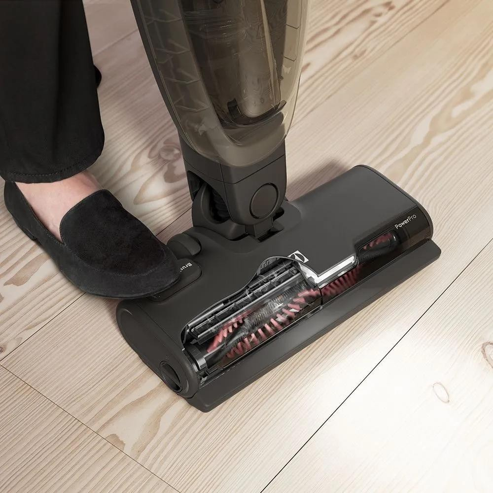 Primo piano del piede di una persona con una scarpa nera accanto a un aspirapolvere.