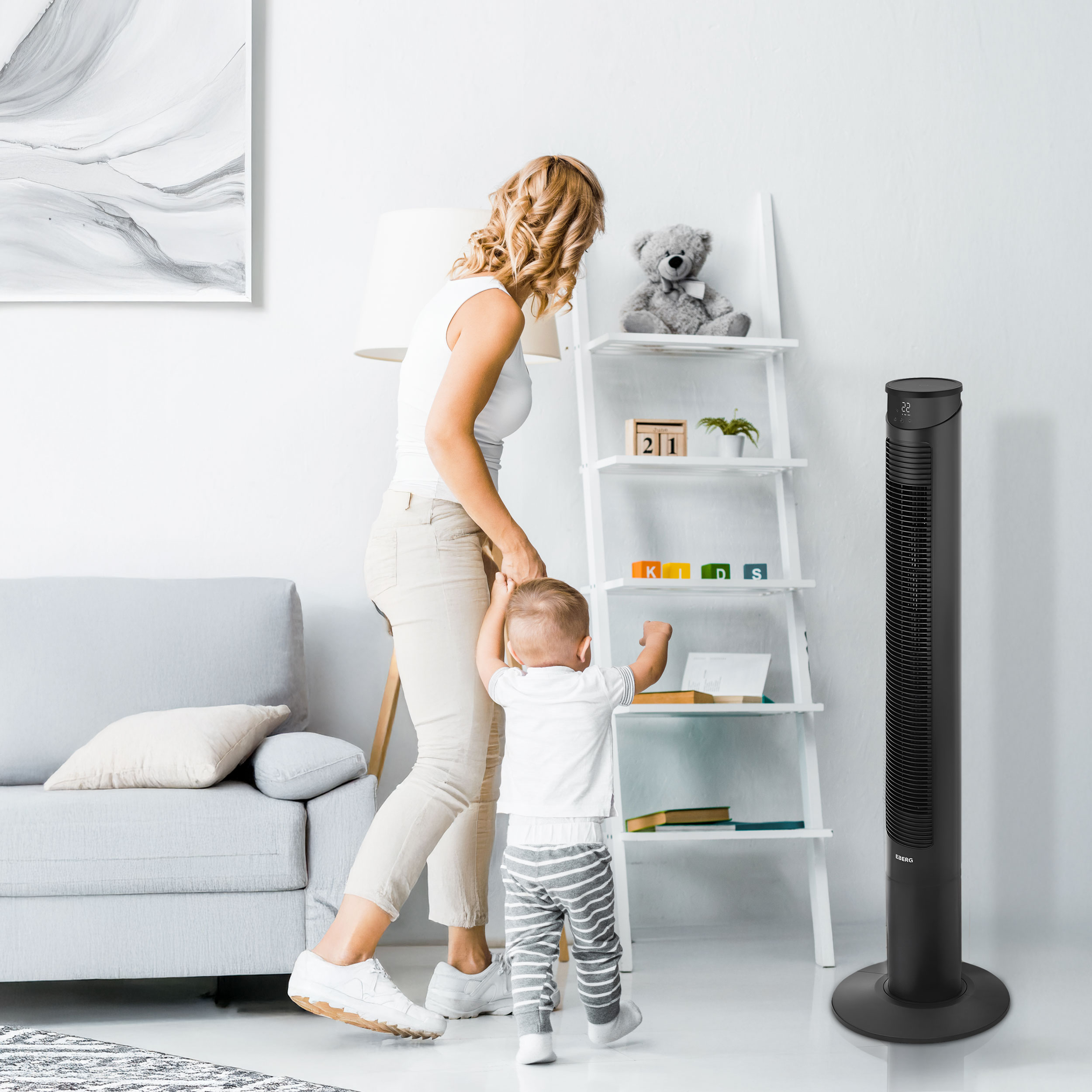 Kobieta trzyma dziecko za rękę, obok stoi wentylator wieżowy.