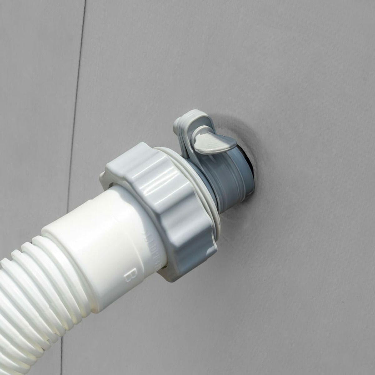 Białe złącze węża z szarymi okuciami jest przymocowane do szarej ściany.