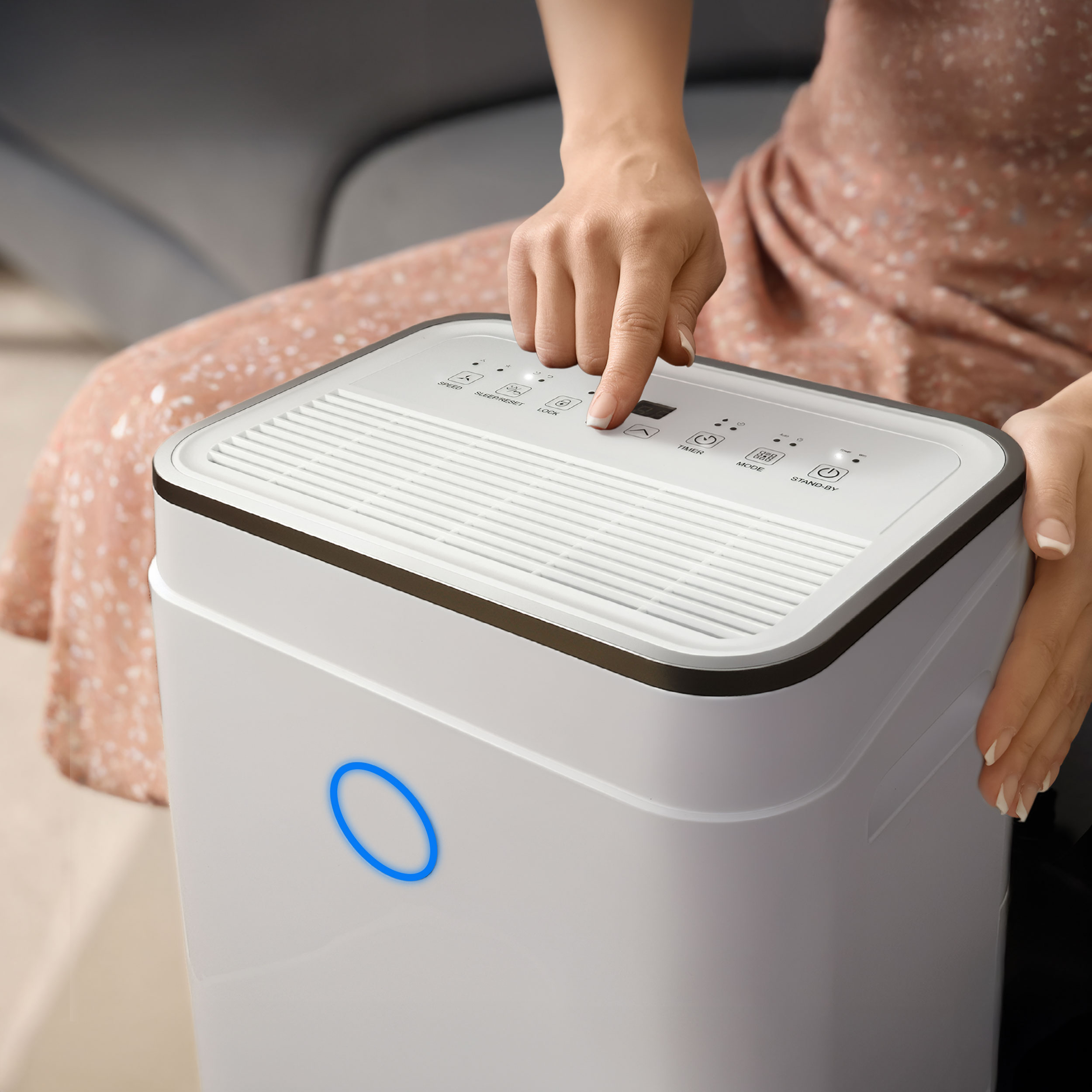 Dłoń naciska przycisk na białym oczyszczaczu powietrza z niebieskim podświetleniem.