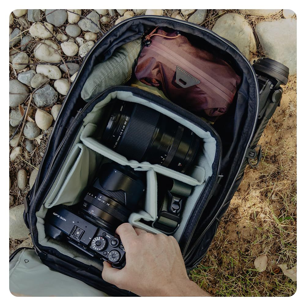 Una mano inserisce una fotocamera Fujifilm GFX 50R nera in uno zaino con attrezzatura fotografica.