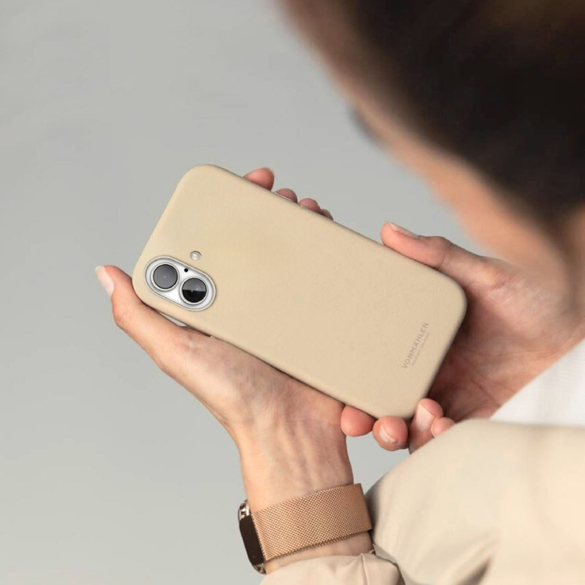 Person hält ein hellbeiges Handy mit zwei Kameras und einem Logo.