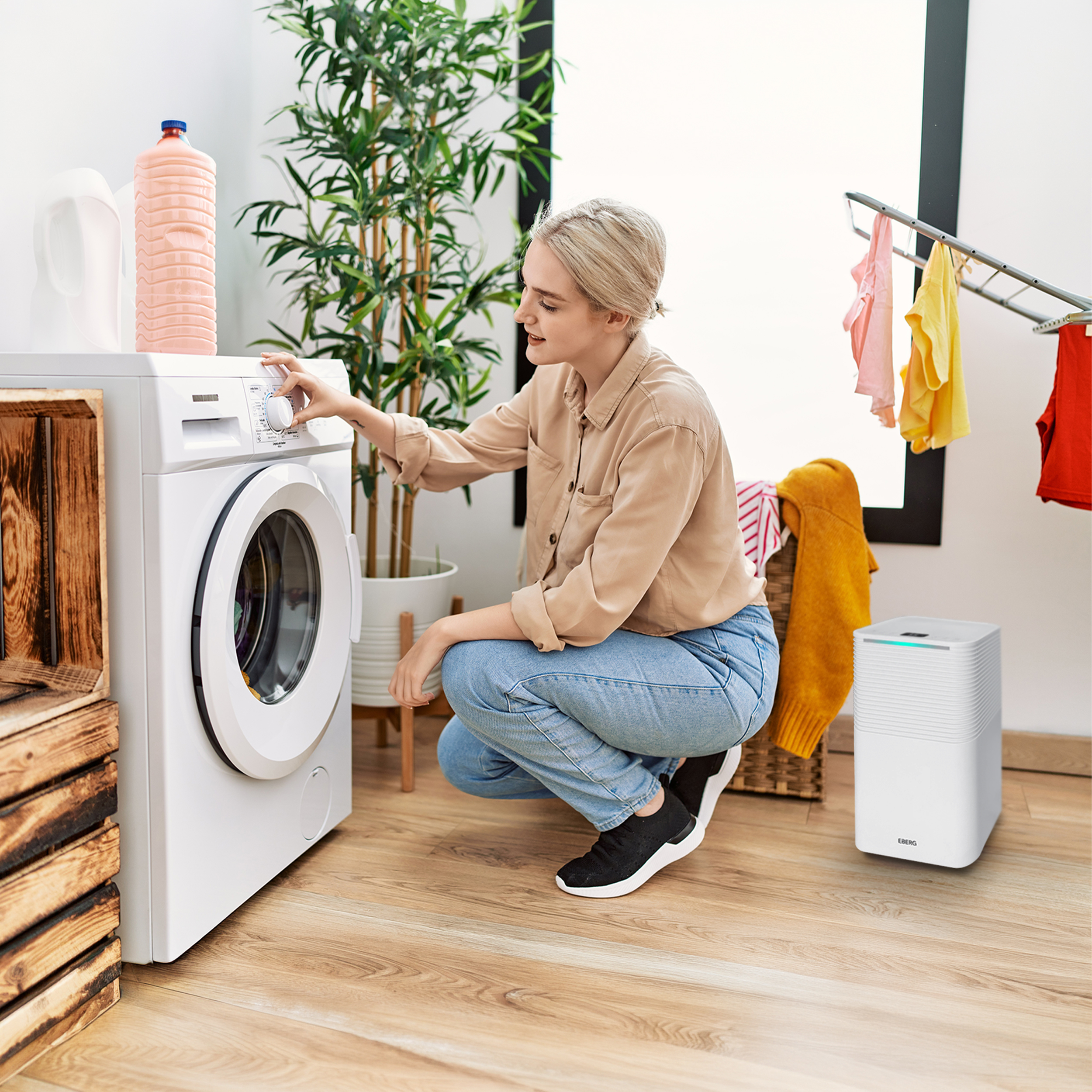 Kobieta z krótkimi blond włosami reguluje pralkę. Obok niej stoi kosz na pranie.