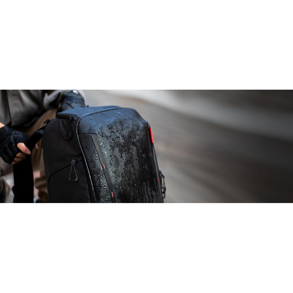 Personne tenant un sac à dos noir mouillé, à l'extérieur avec un fond flou.