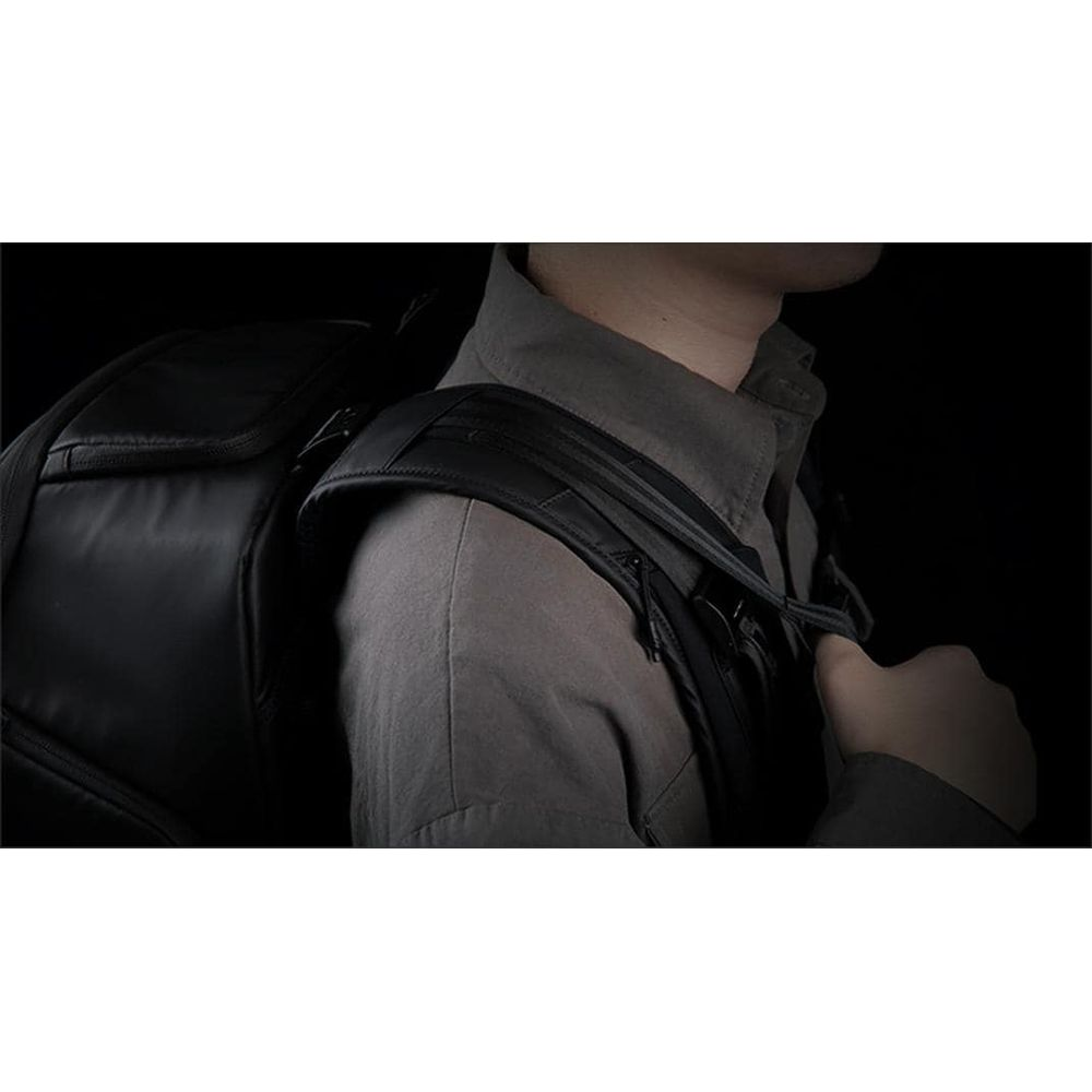 Personne portant un sac à dos noir sur fond sombre.