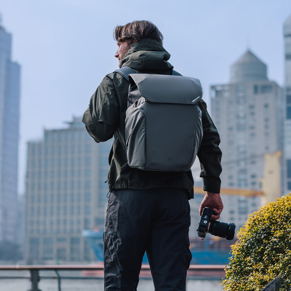 Homme avec sac à dos et appareil photo en ville, bâtiments en arrière-plan.