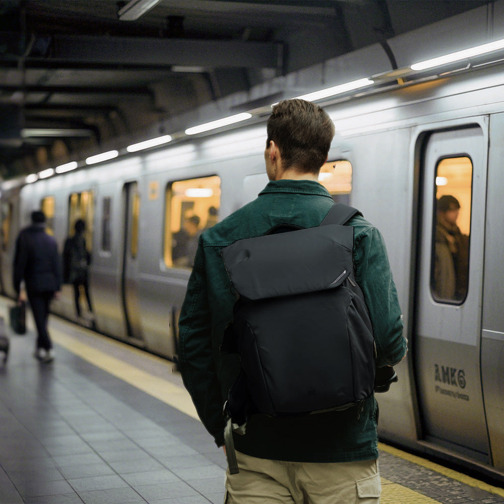 Homme avec sac à dos noir attendant un train dans une station de métro.