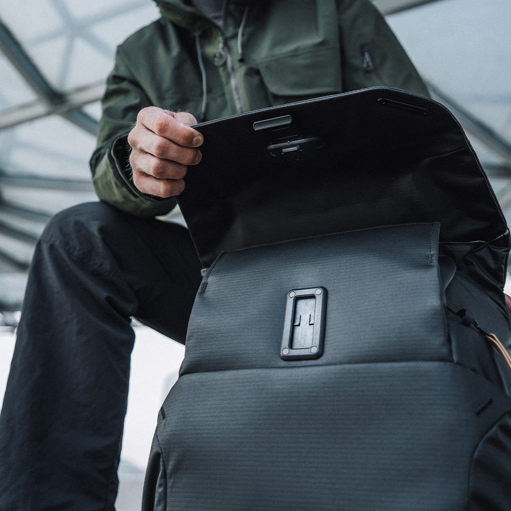 Une personne ouvre un sac noir, portant une veste verte à capuche.