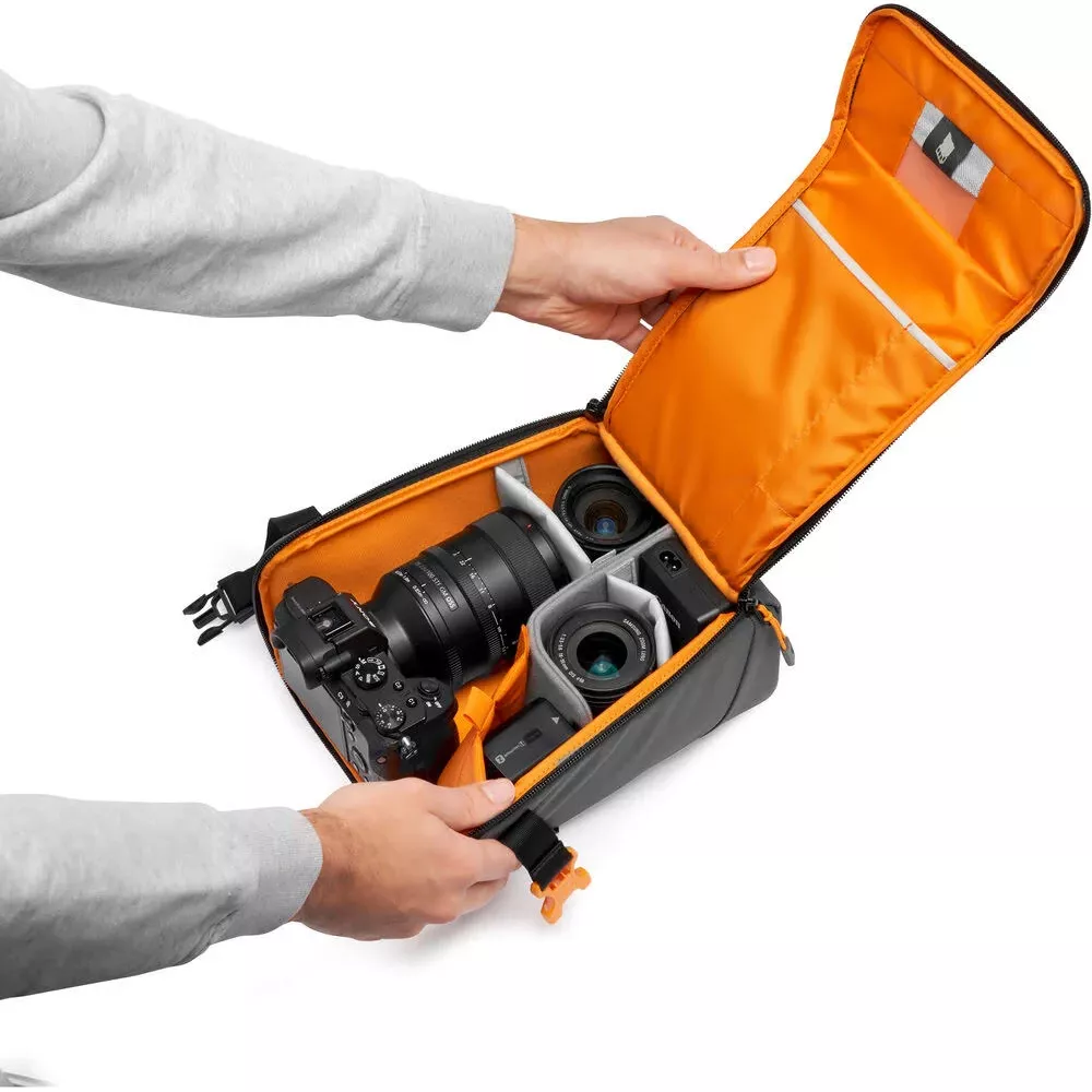 Una persona sistema fotocamera, obiettivi e accessori in una borsa fotografica foderata di arancione.