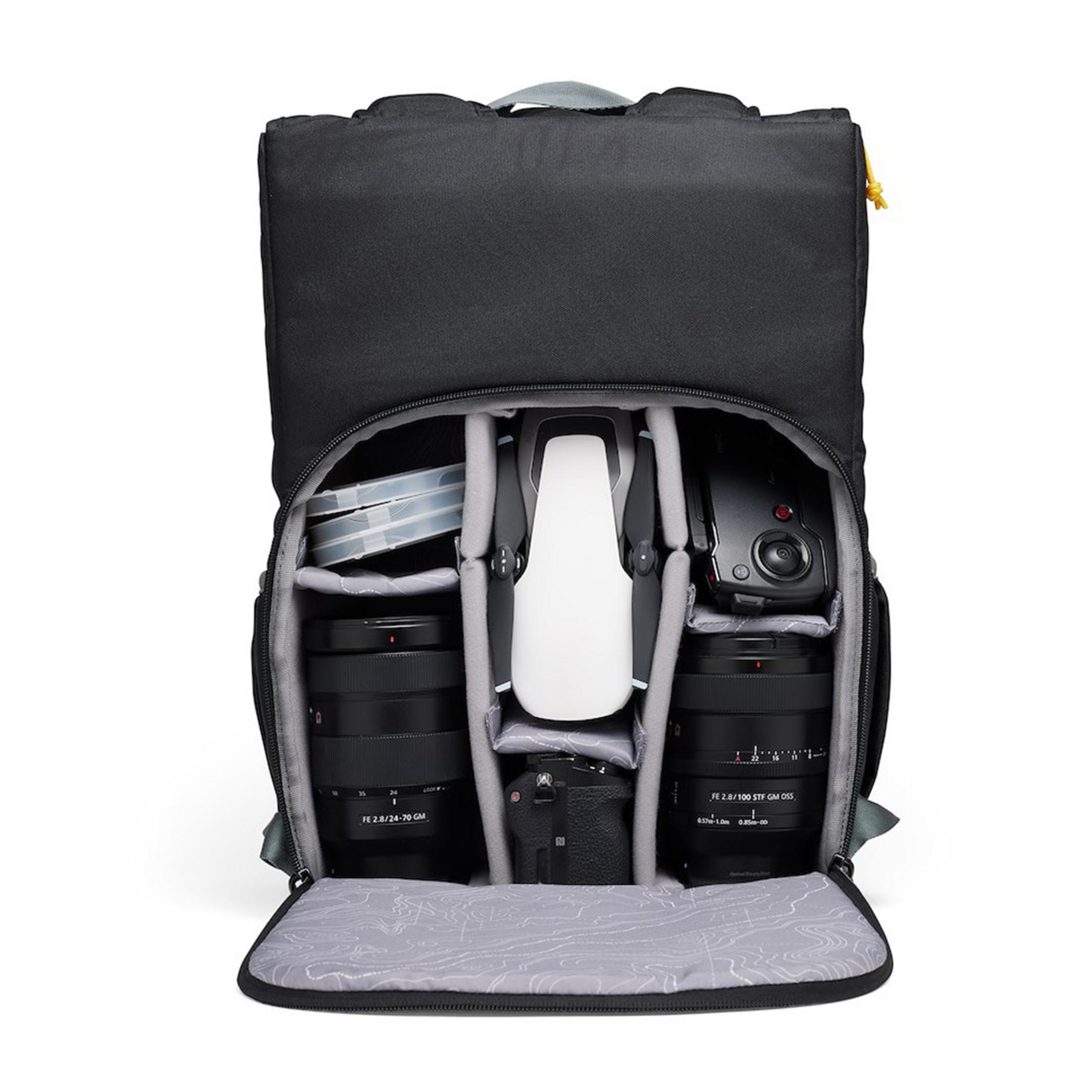 Un sac à dos noir est ouvert, montrant un drone, des caméras et des objectifs.
