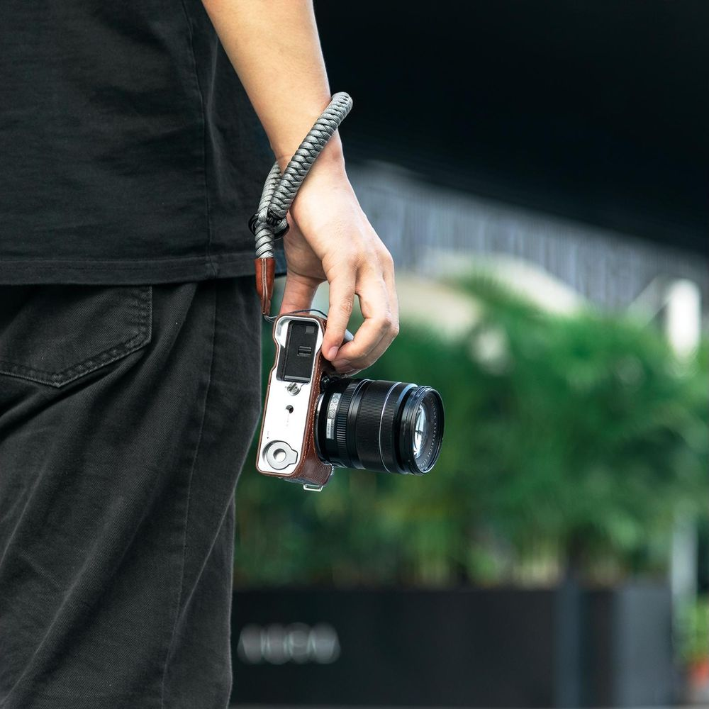 Una persona in maglietta nera tiene una fotocamera con custodia in pelle marrone e laccetto.