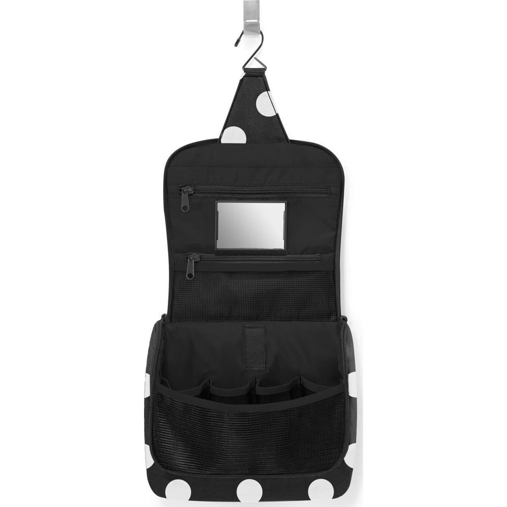 Schwarze Kulturtasche mit weißen Punkten, aufgehängt an einem Haken. Offen mit Fächern.