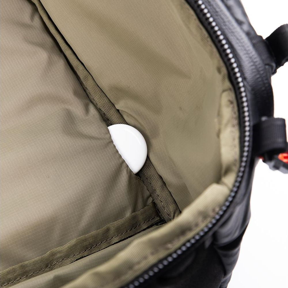 Un objet blanc semi-circulaire dépasse de la poche d'un sac noir.