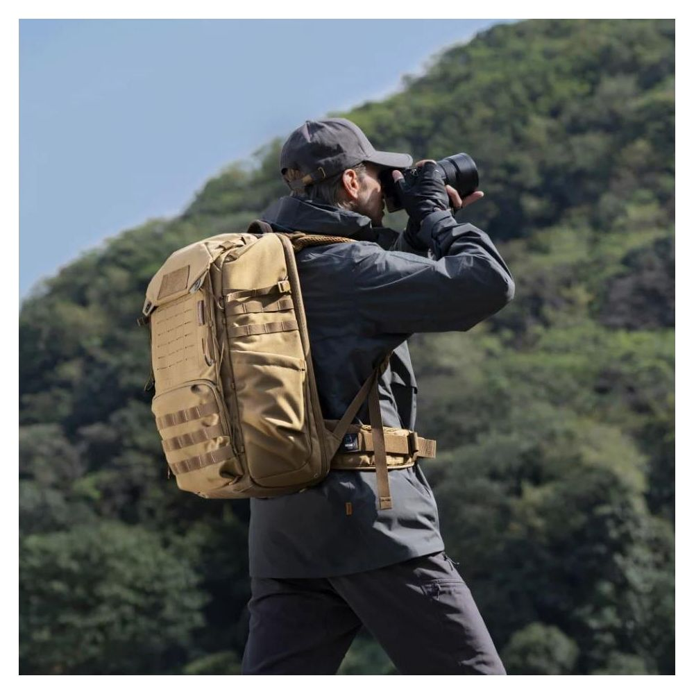 Un homme avec un sac à dos prend une photo dans un paysage vallonné et boisé.