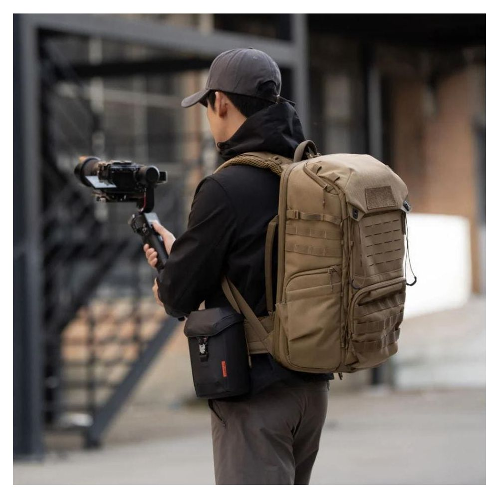 Homme avec sac à dos et cardan en main, debout dehors.
