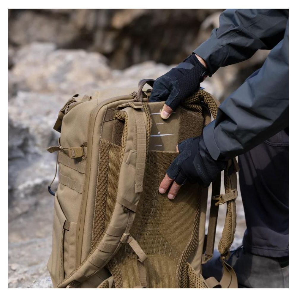 Personne en veste sombre et gants ajuste un sac à dos beige avec panneau arrière en maille.