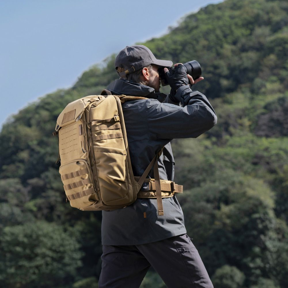Un homme avec un sac à dos prend des photos dans un paysage montagneux.