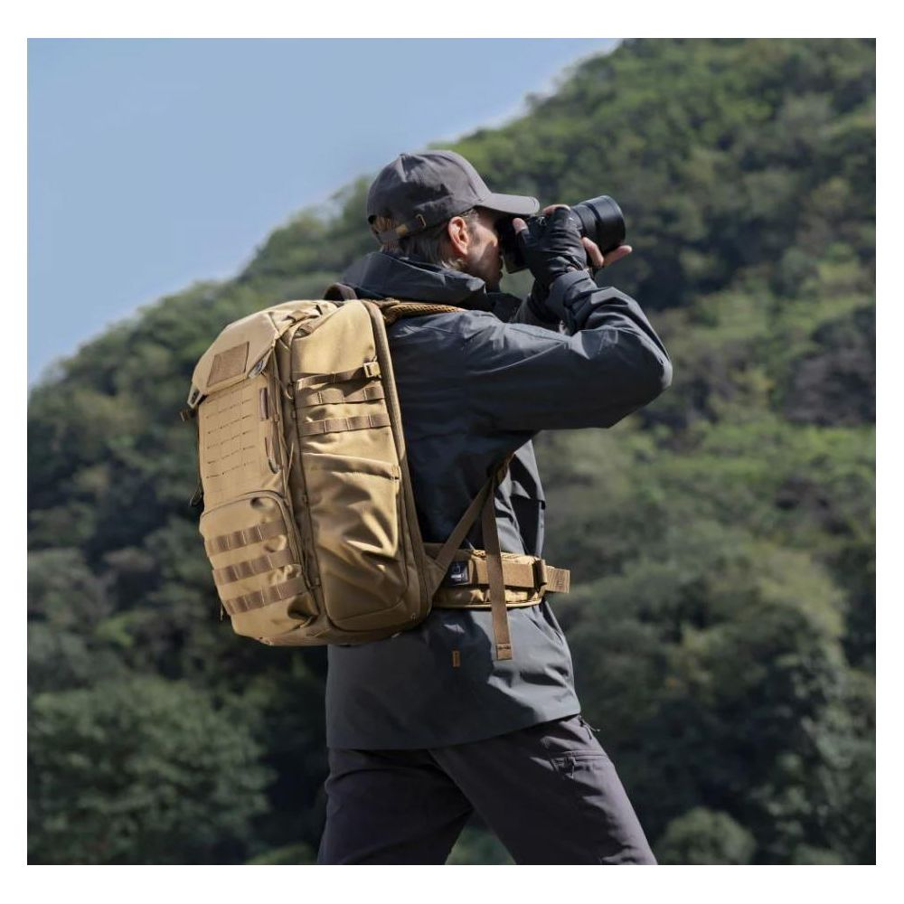 Homme avec sac à dos tactique photographie devant un paysage verdoyant.