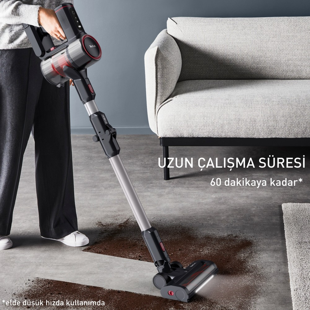 Bir kişi kanepe yanında kablosuz süpürge ile kir süpürüyor.