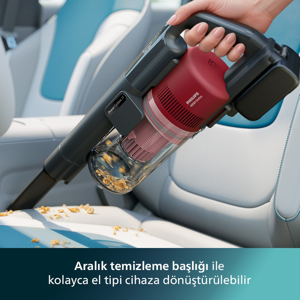 Bir el, araba koltuğundaki kırıntıları süpüren kırmızı bir el süpürgesi tutuyor.