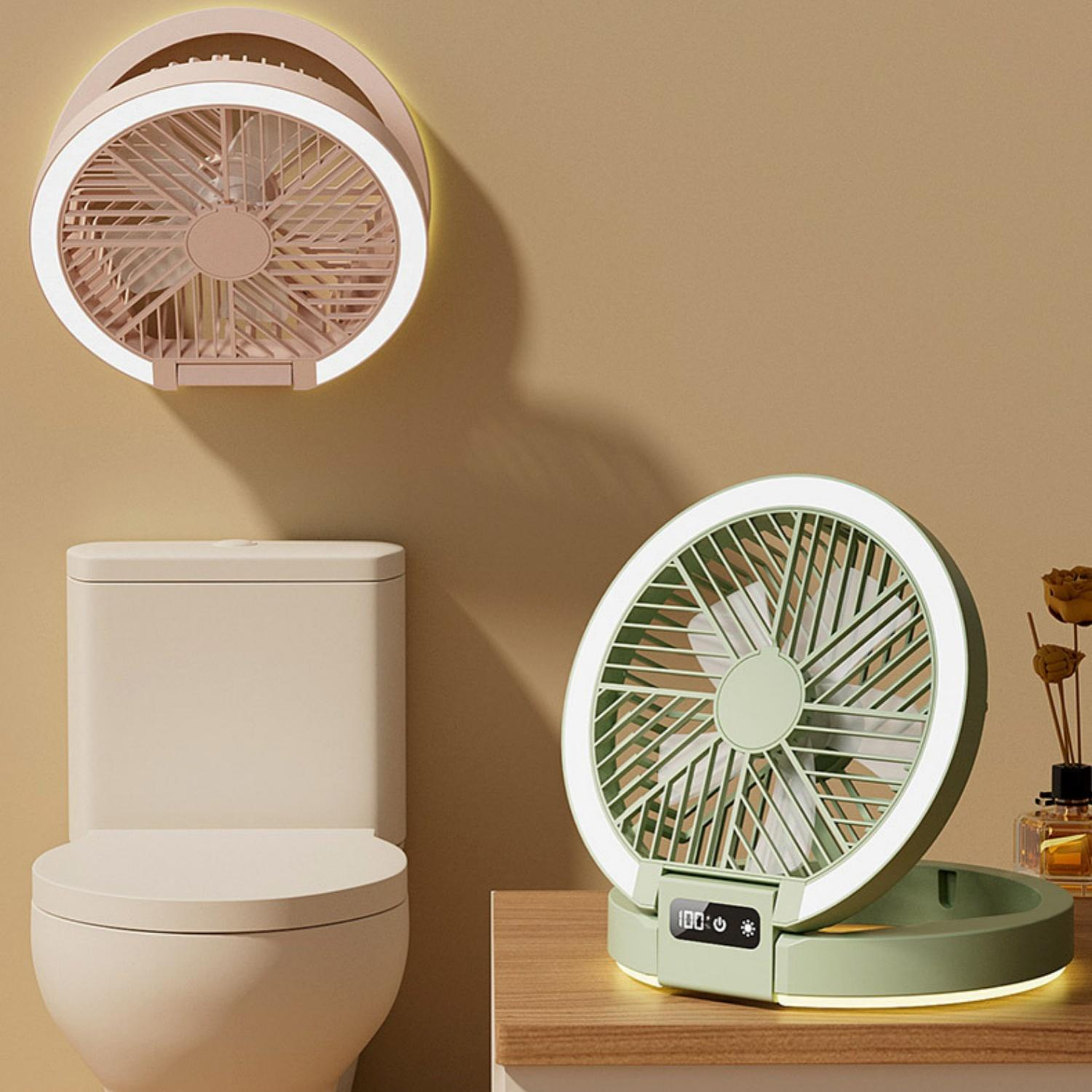 Ein rosa Ventilator mit Licht hängt an der Wand neben einer Toilette. Ein grünes Ventilator steht auf einem Tisch.