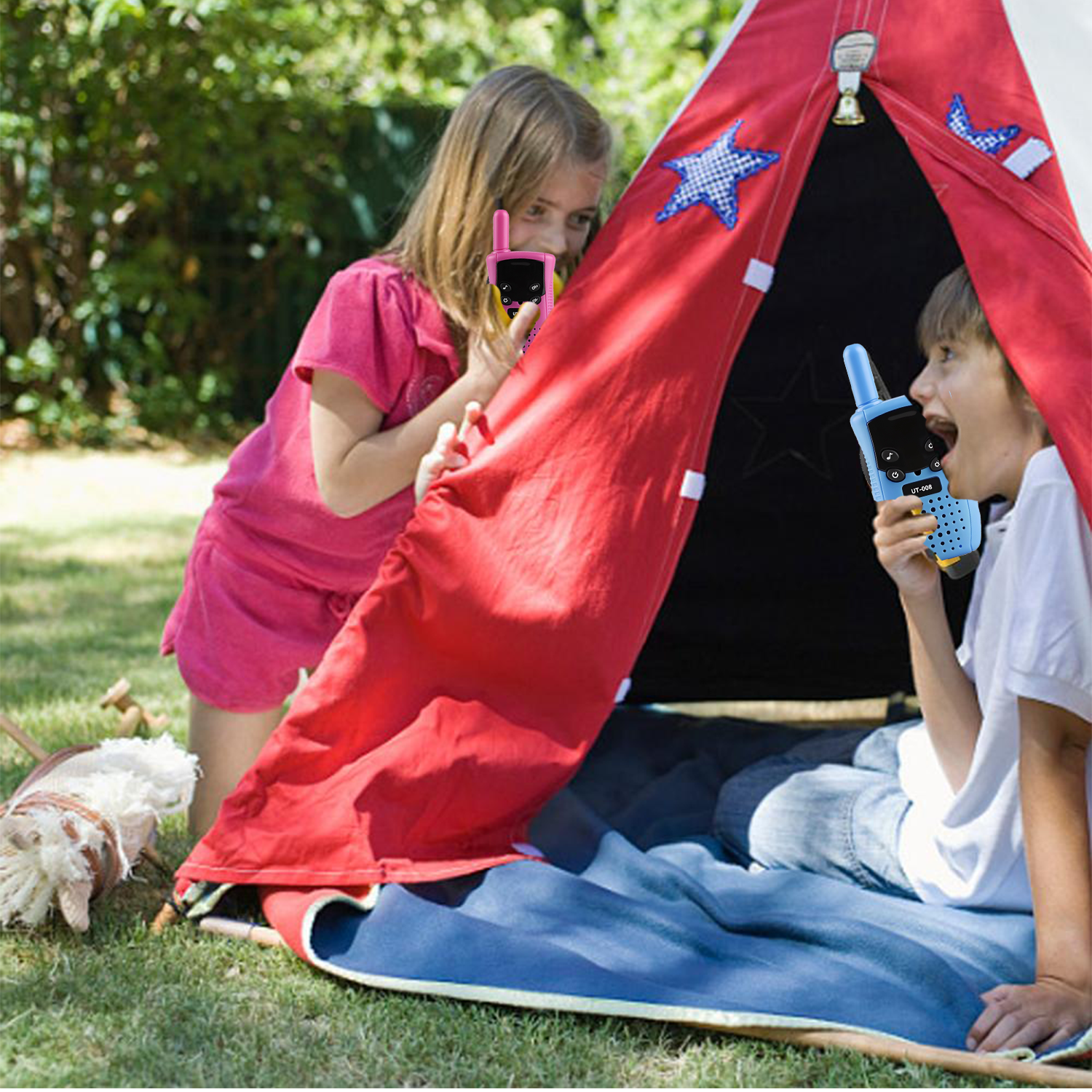 Zwei Kinder spielen mit Walkie-Talkies vor einem roten Zelt im Freien.
