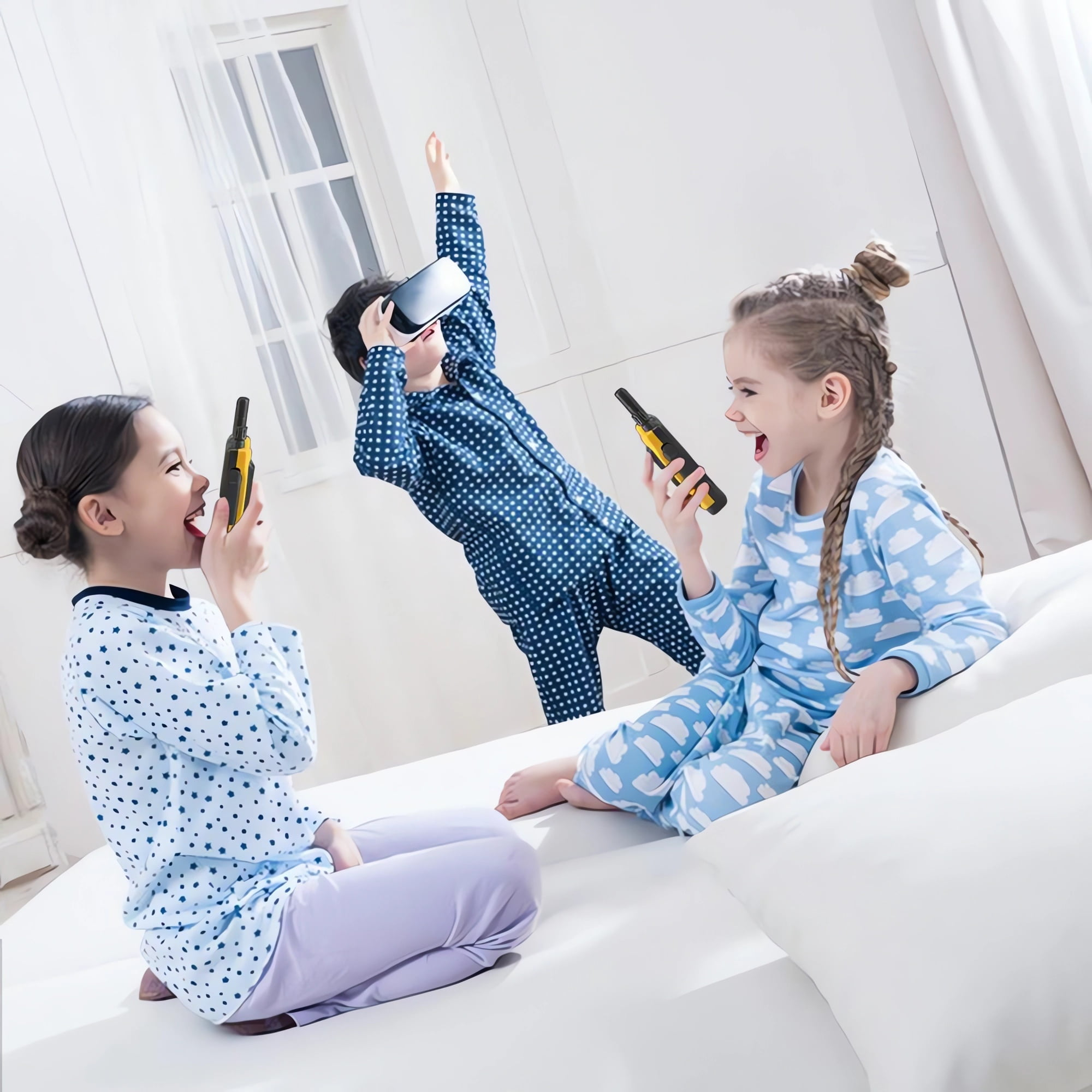 Drei Kinder in Schlafanzügen auf einem Bett, zwei halten Walkie-Talkies, eines trägt VR-Brille.