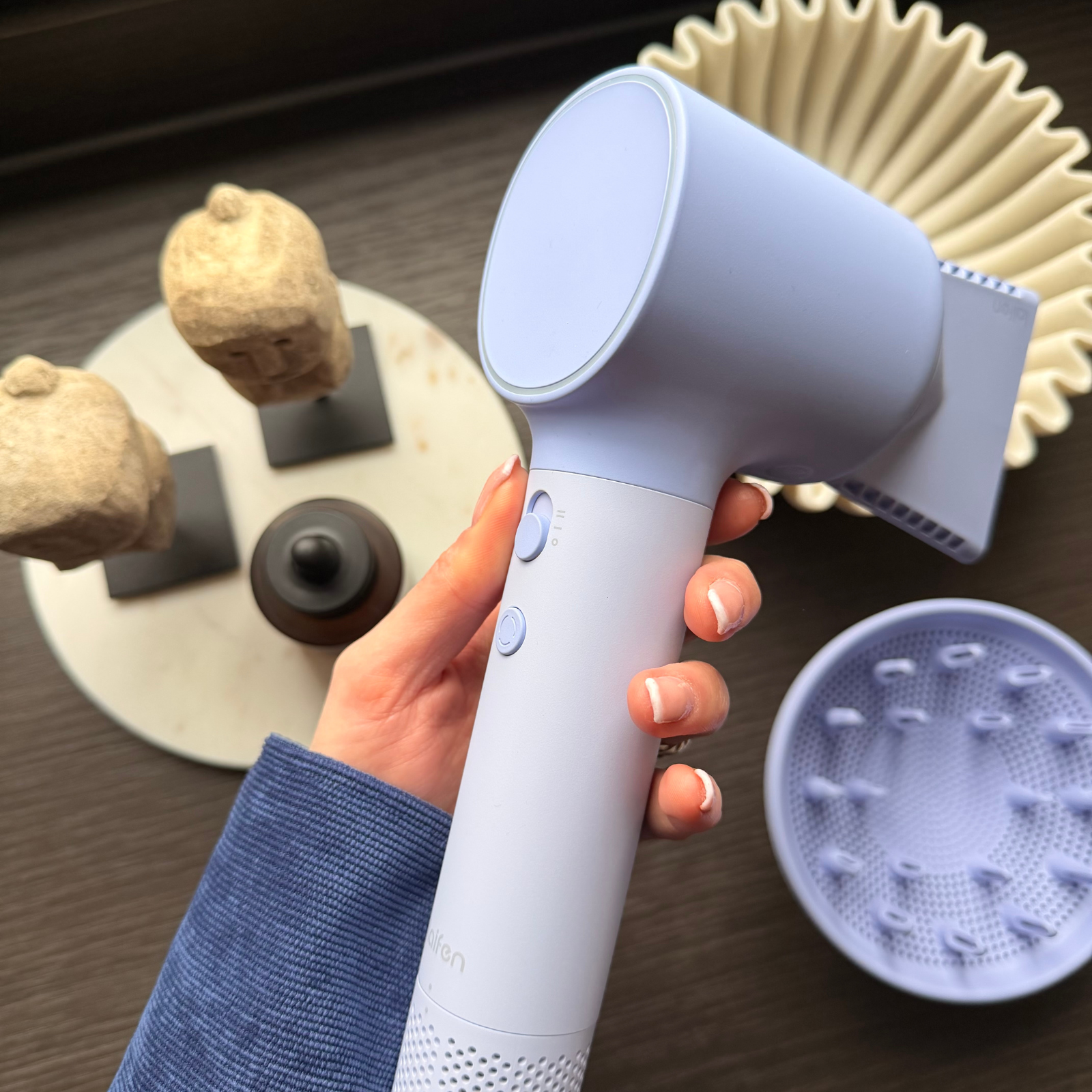 Eine Hand hält einen lavendelfarbenen Haartrockner mit einem Diffusor daneben.
