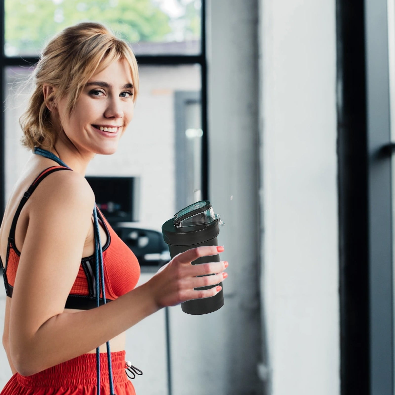 Eine Frau mit blonden Haaren in Sportkleidung hält eine schwarze Wasserflasche.
