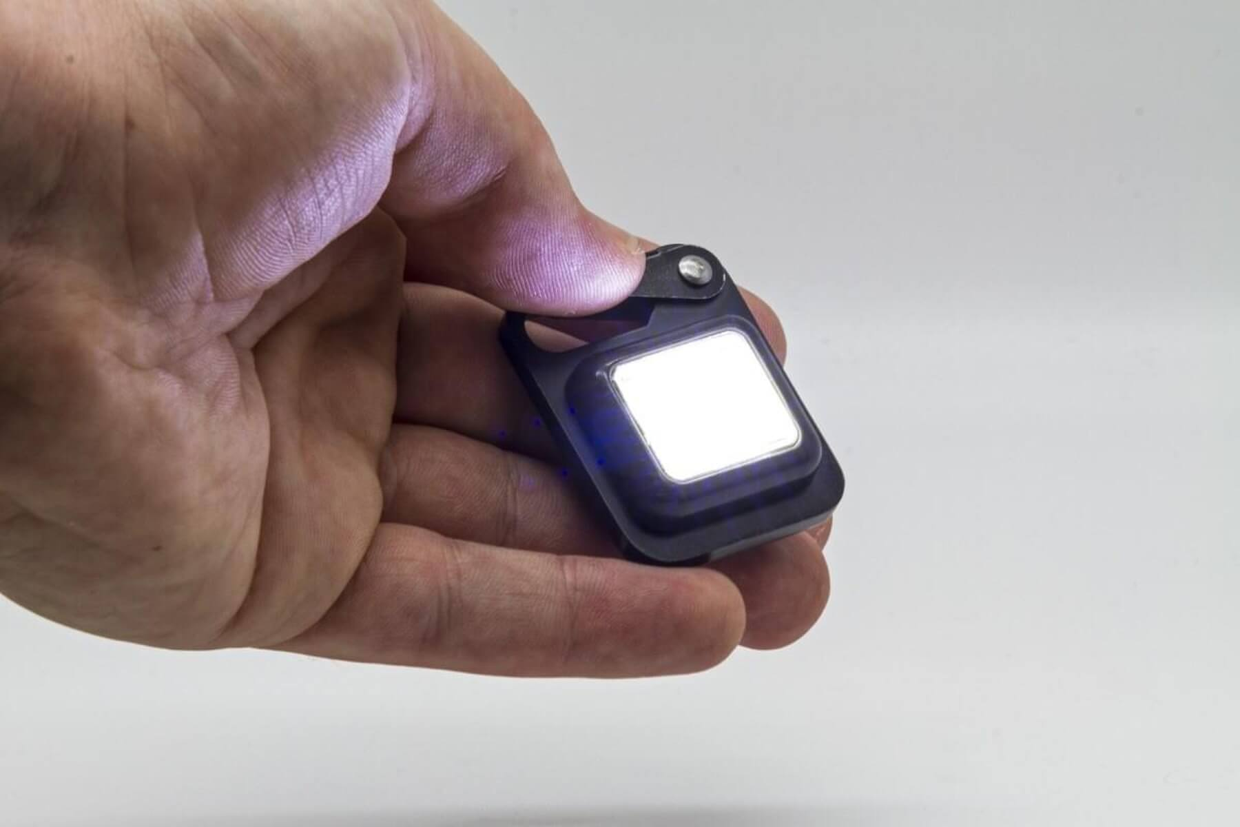 Una mano tiene una piccola torcia quadrata che emette una luce brillante.