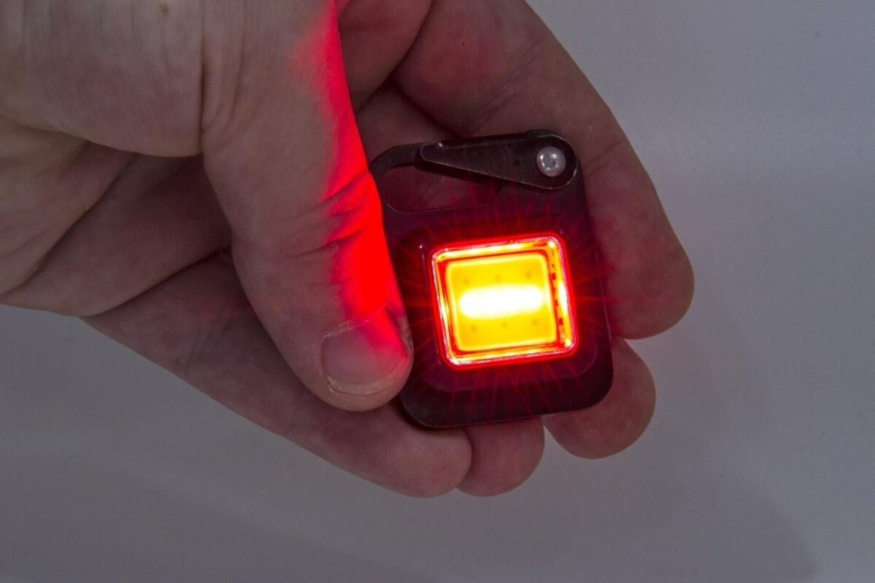 Luce rossa brilla su una mano che tiene una piccola luce illuminata per portachiavi.