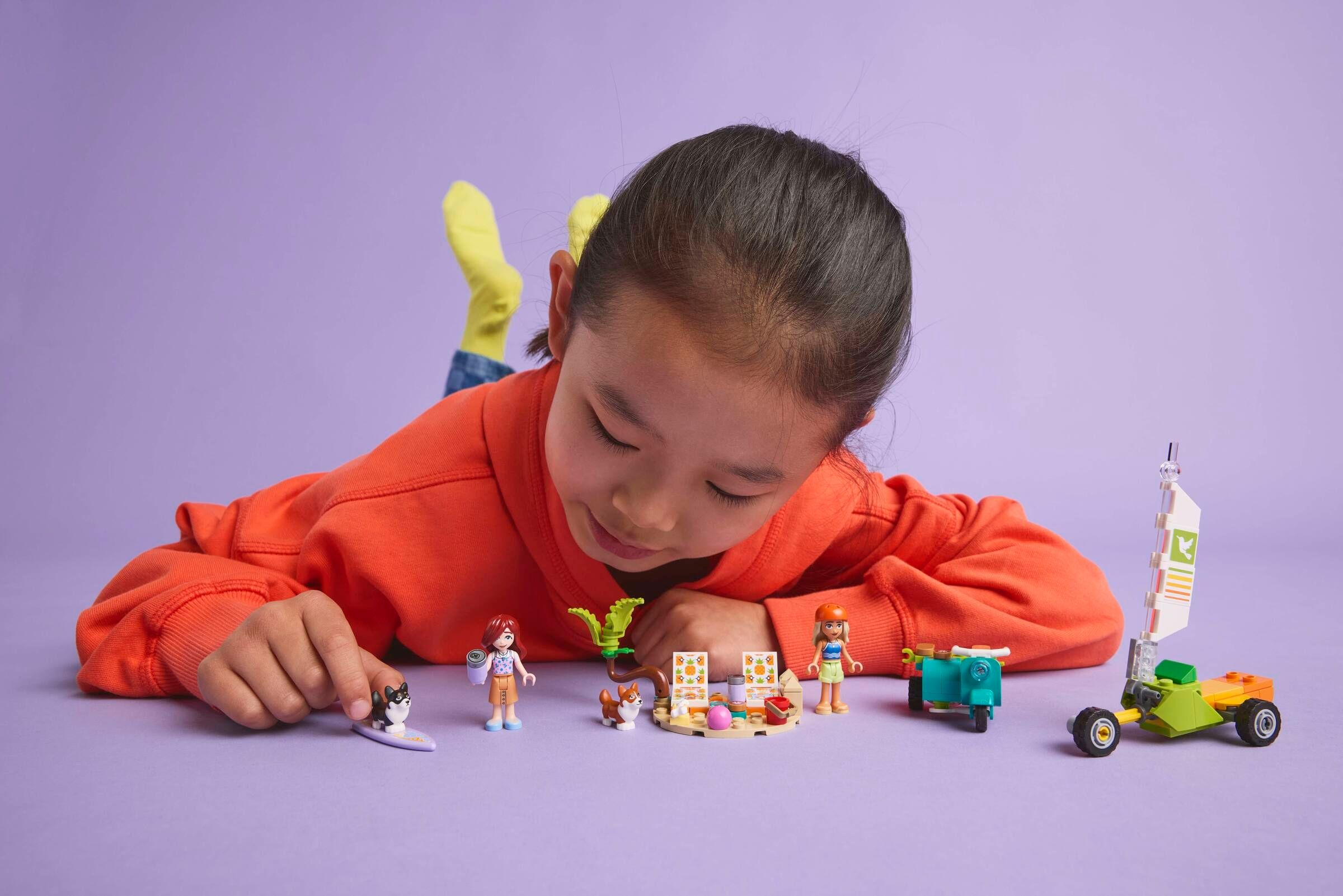 Ein Mädchen spielt mit Lego-Figuren und Tieren auf lila Untergrund.