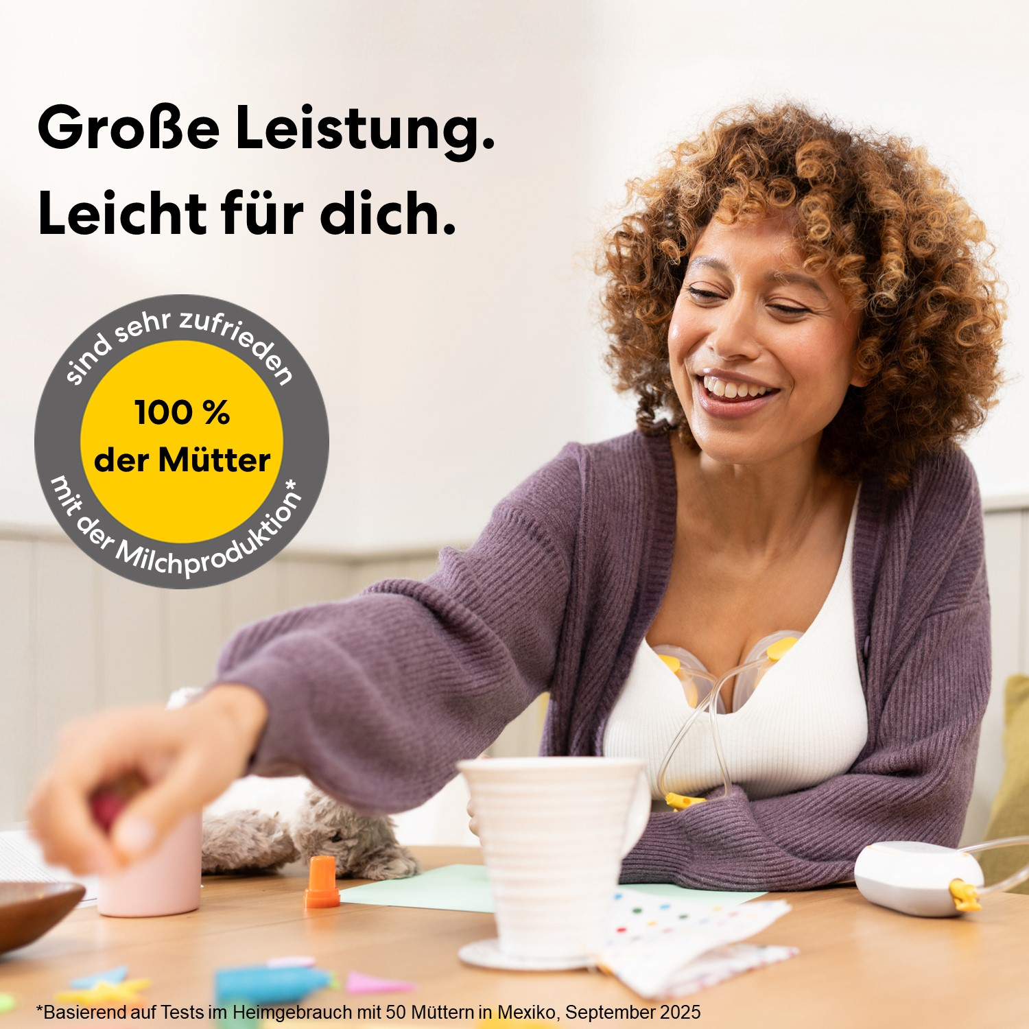 Eine Frau mit lockigem Haar lächelt, während sie eine Milchpumpe trägt. Ein Kreis mit Text ist im Vordergrund.
