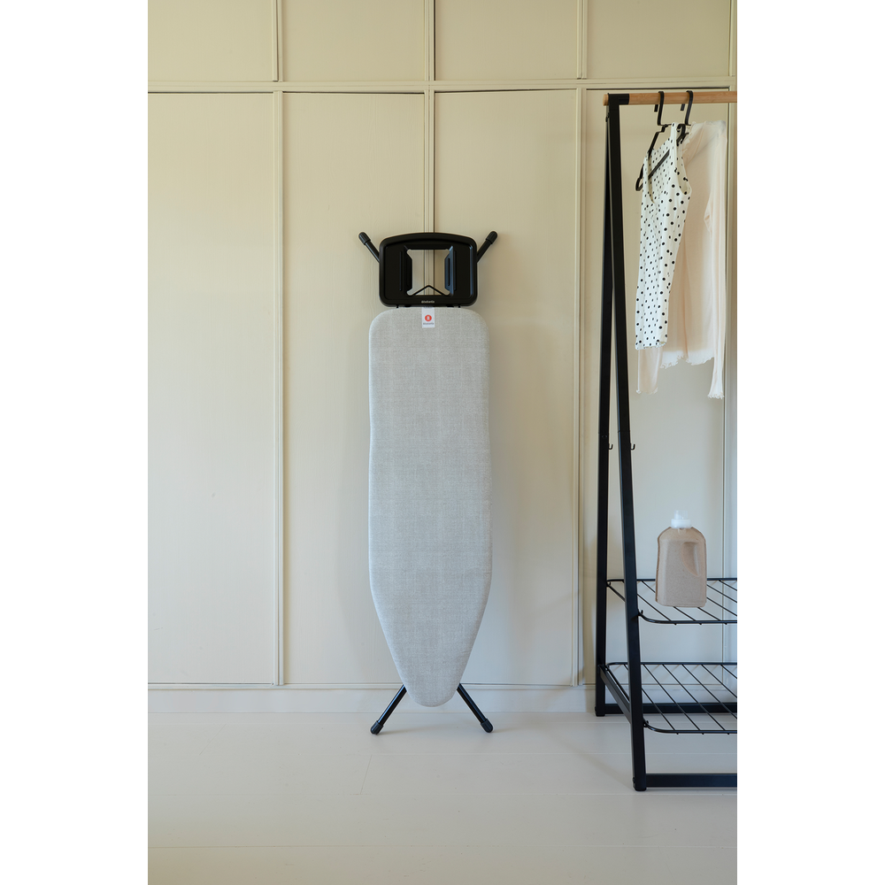 Une planche à repasser devant un mur avec portant à vêtements et vêtements.