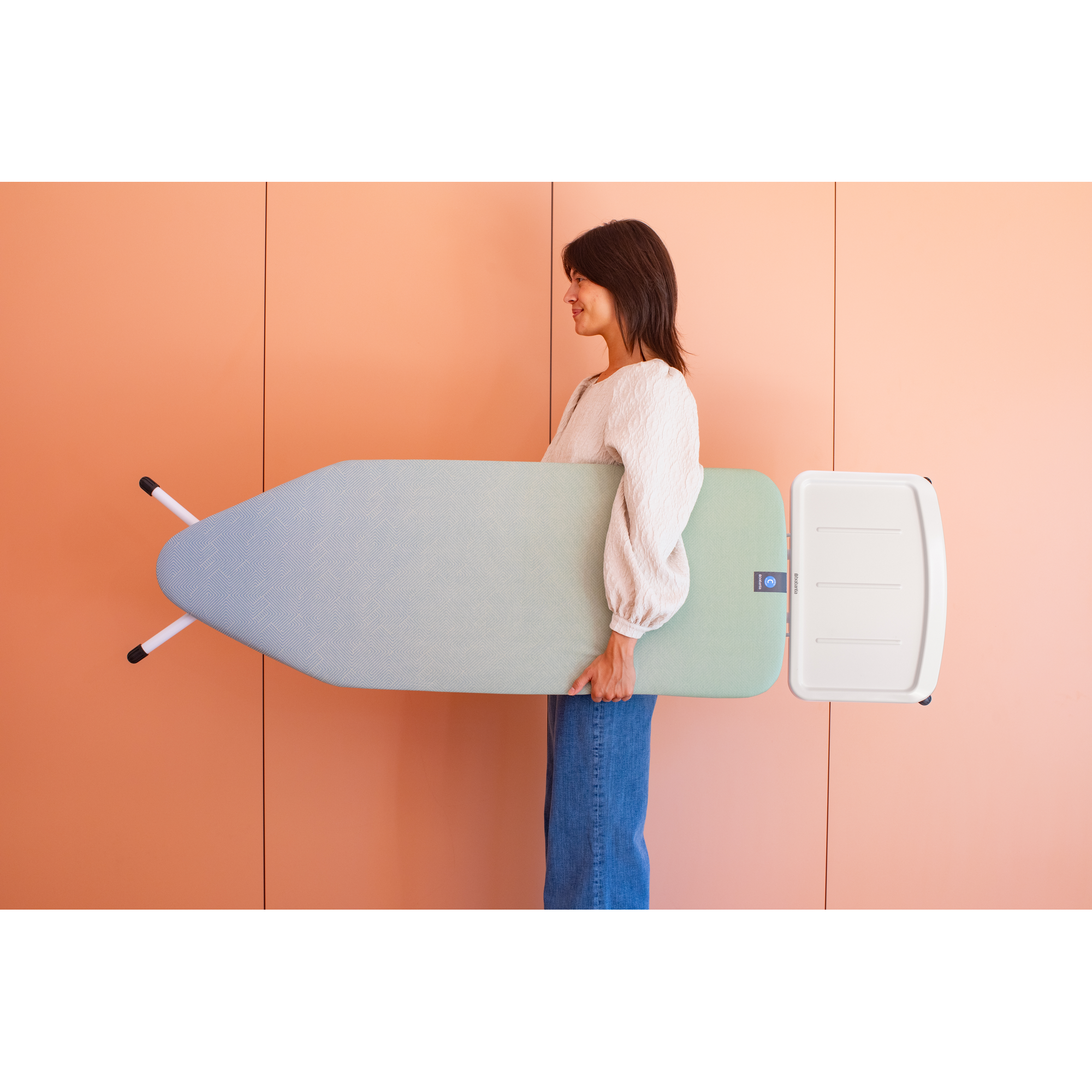 Een vrouw in jeans draagt een strijkplank met een witte bevestiging.