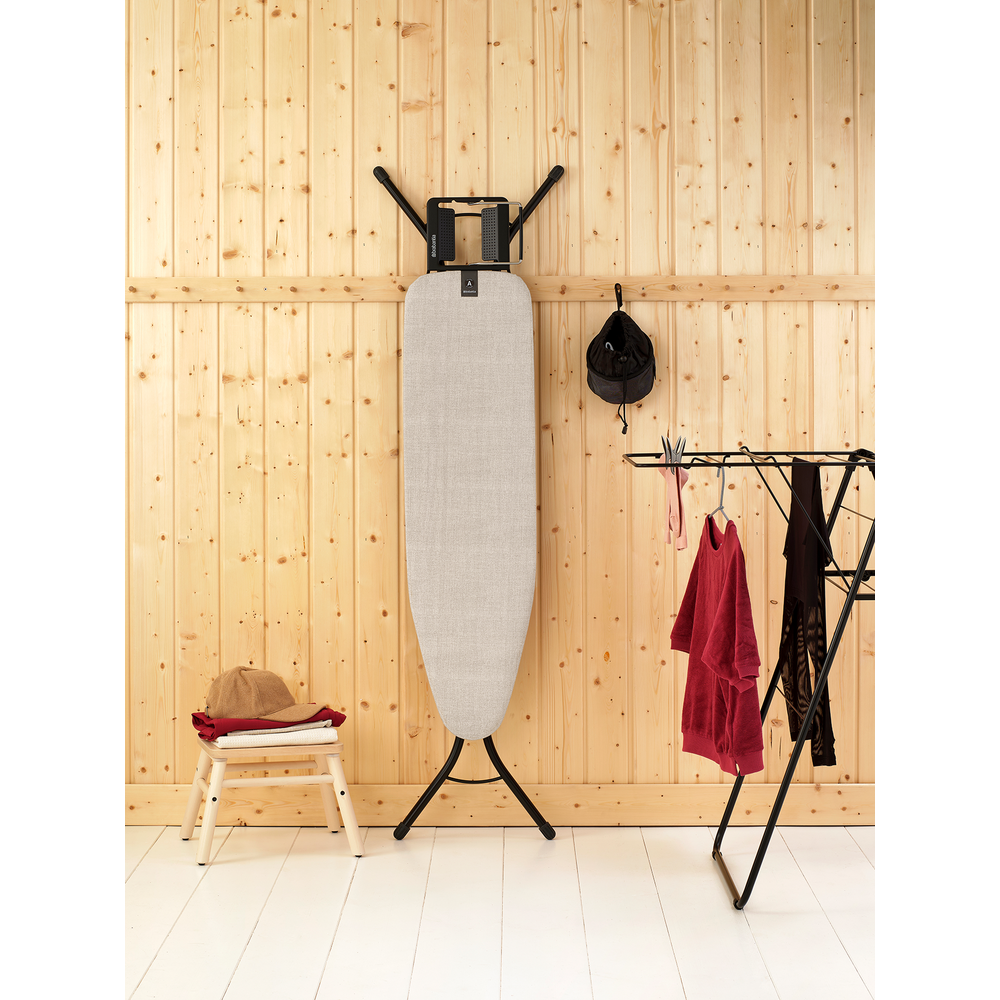 Une planche à repasser est contre un mur en bois. Du linge est suspendu sur un étendoir.