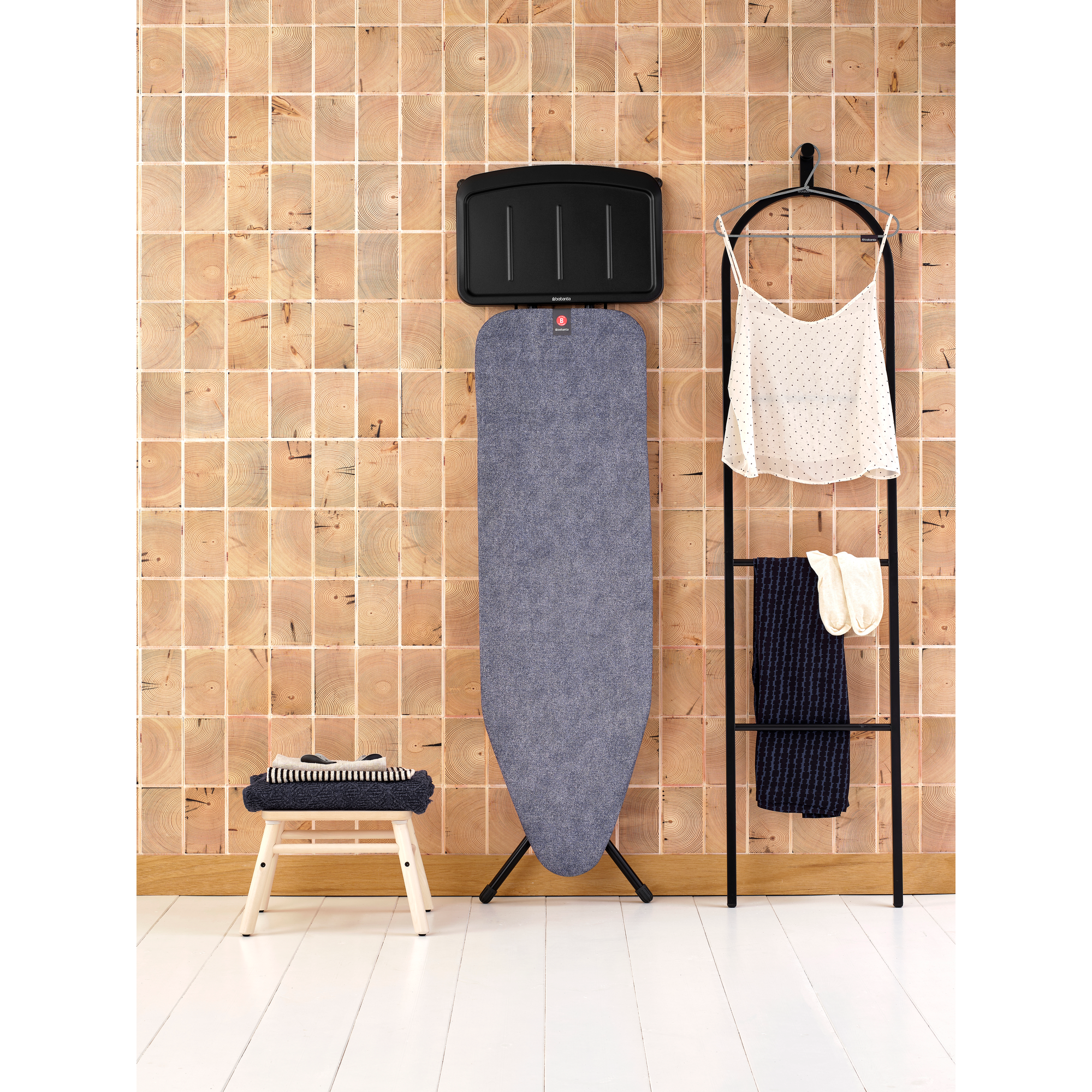 Table à repasser, vêtements et tabouret devant mur en bois.