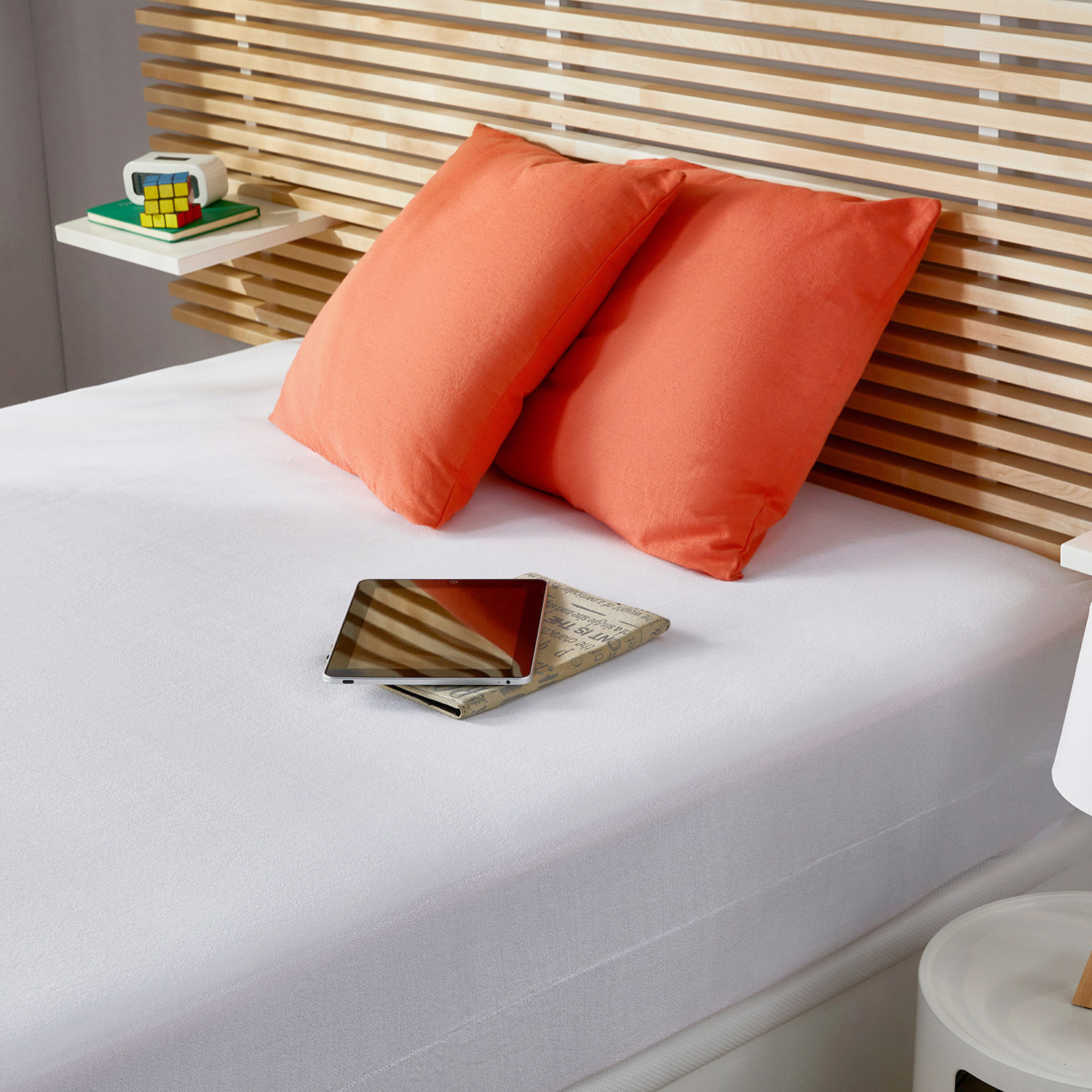Una cama con almohadas naranjas, una tablet y un cubo de Rubik.