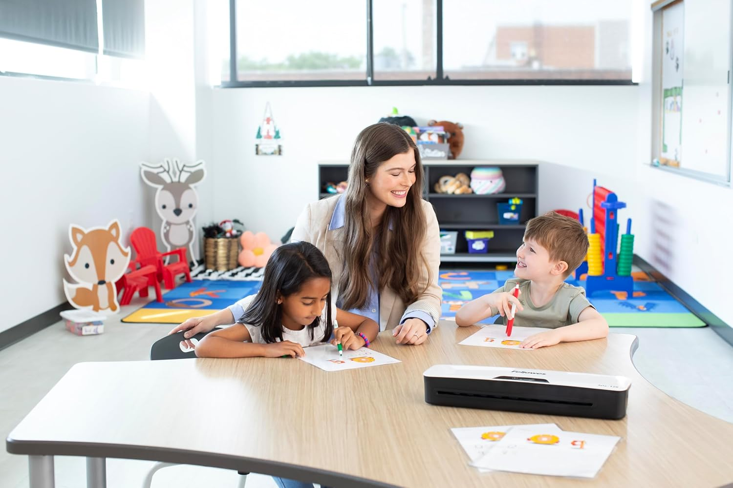 Lehrerin hilft Kindern beim Malen am Tisch in einem Klassenzimmer mit Tierdekorationen.