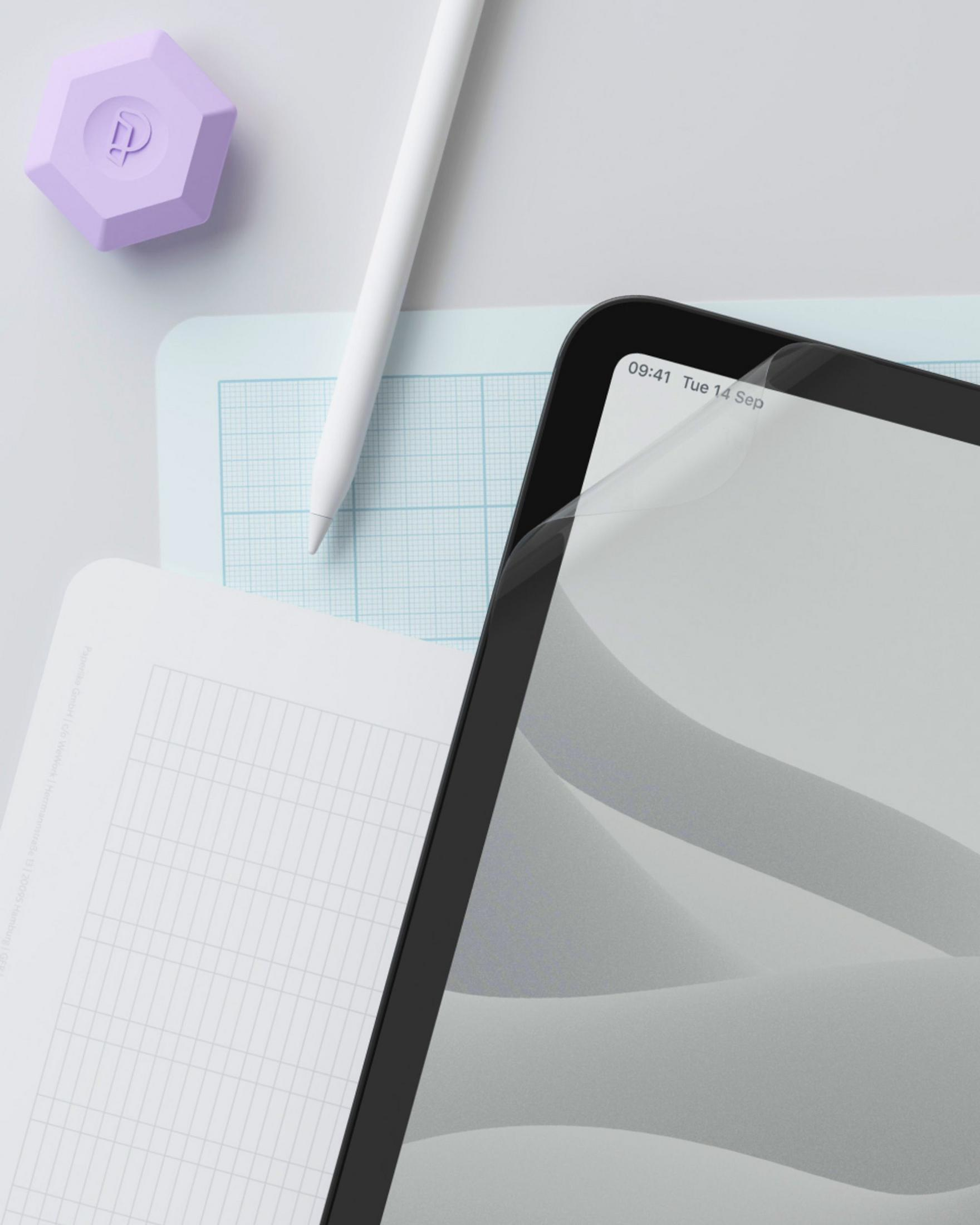 Ein lila Objekt, Stift, Tablet und Papier mit Raster liegen auf einem Tisch.