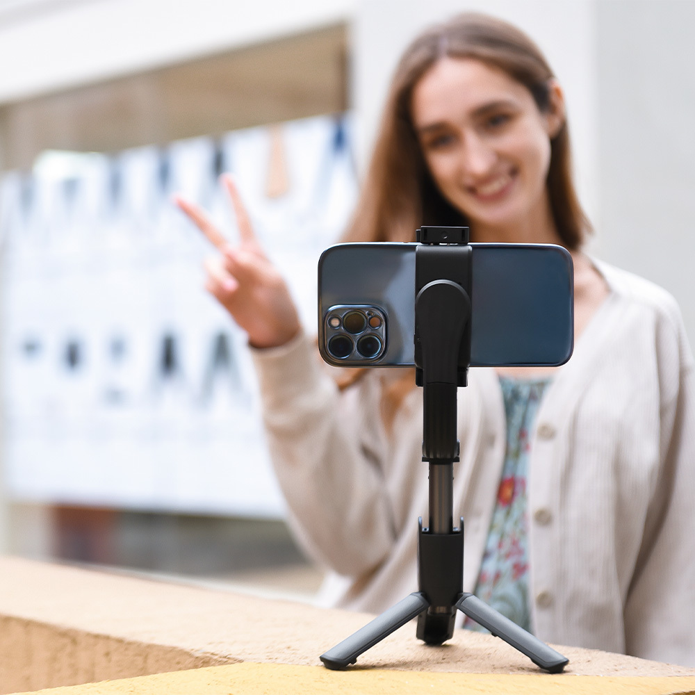 Kobieta robi sobie selfie telefonem na statywie, pokazując znak pokoju.