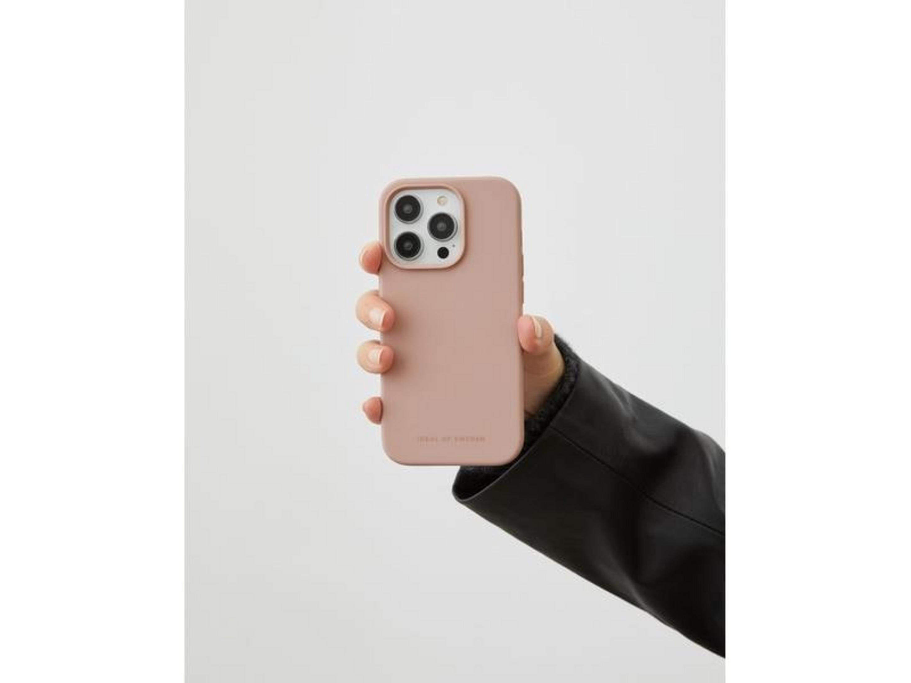 Bir el, açık renkli bir arka plan önünde kamera lensli pembe telefon kılıfı tutuyor.