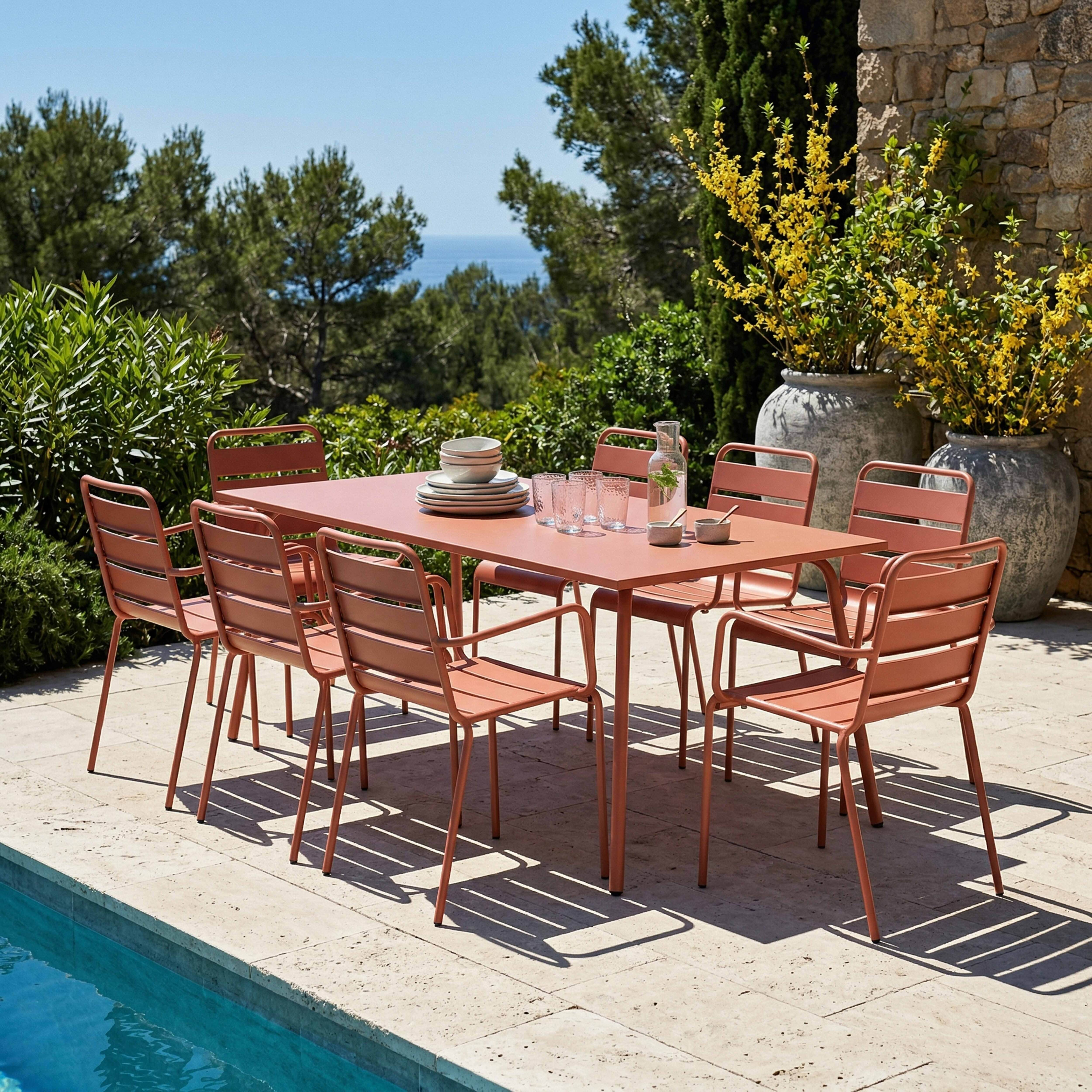 Ein rosafarbener Esstisch mit acht Stühlen steht auf einer Terrasse neben einem Pool.