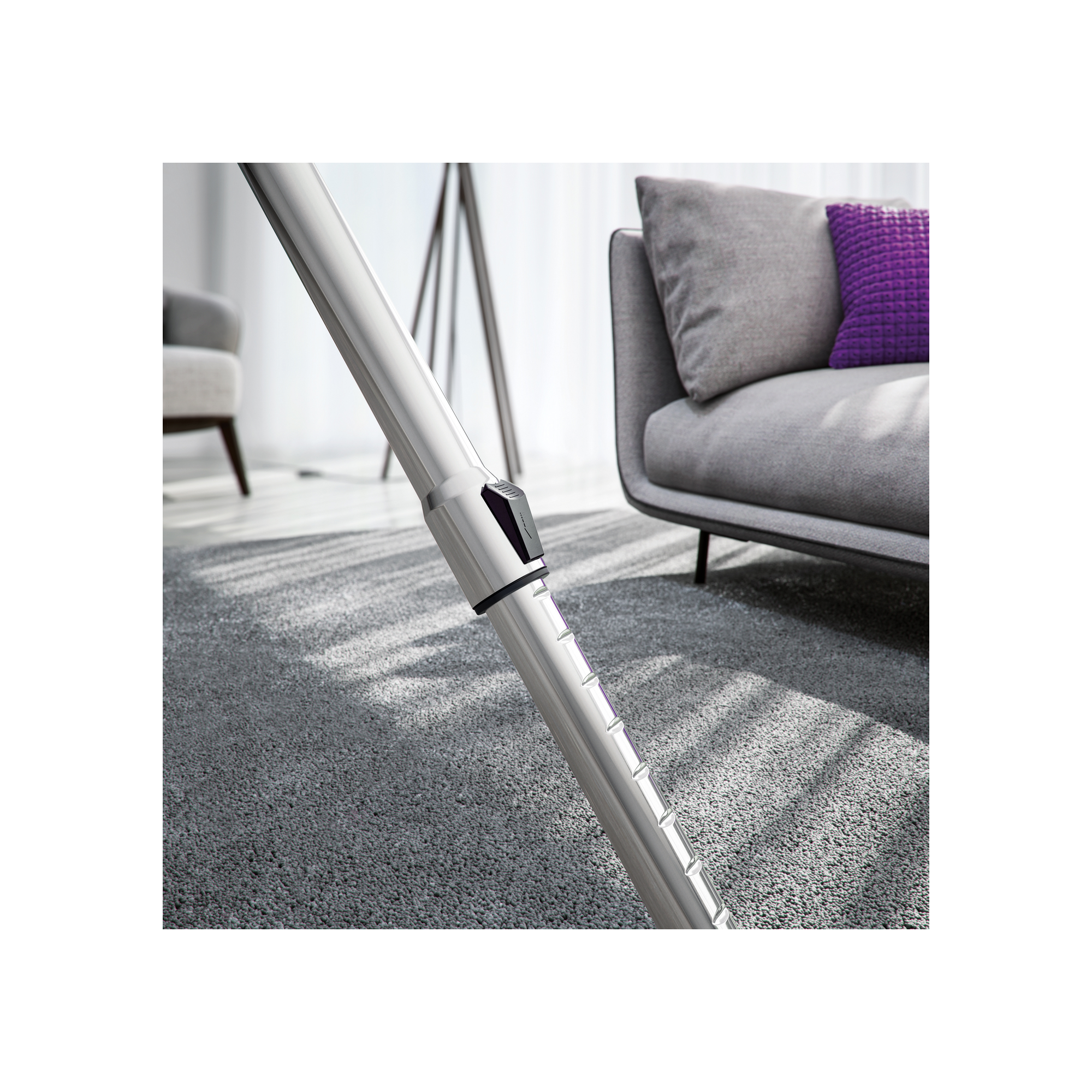 Primer plano de un tubo de aspiradora plateado sobre una alfombra gris con sombras de una ventana.