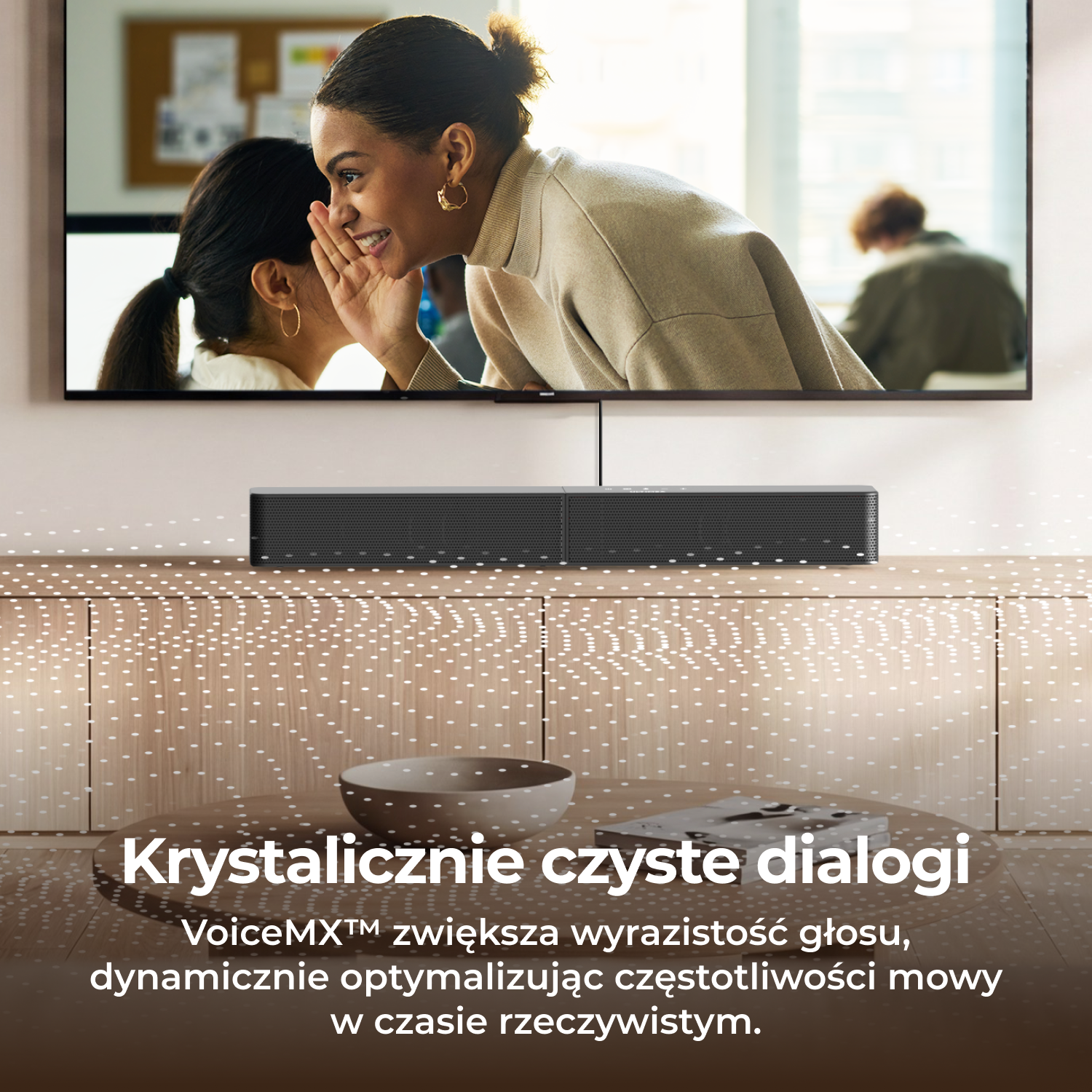 Dwie kobiety szepczą przed telewizorem z soundbarem poniżej.