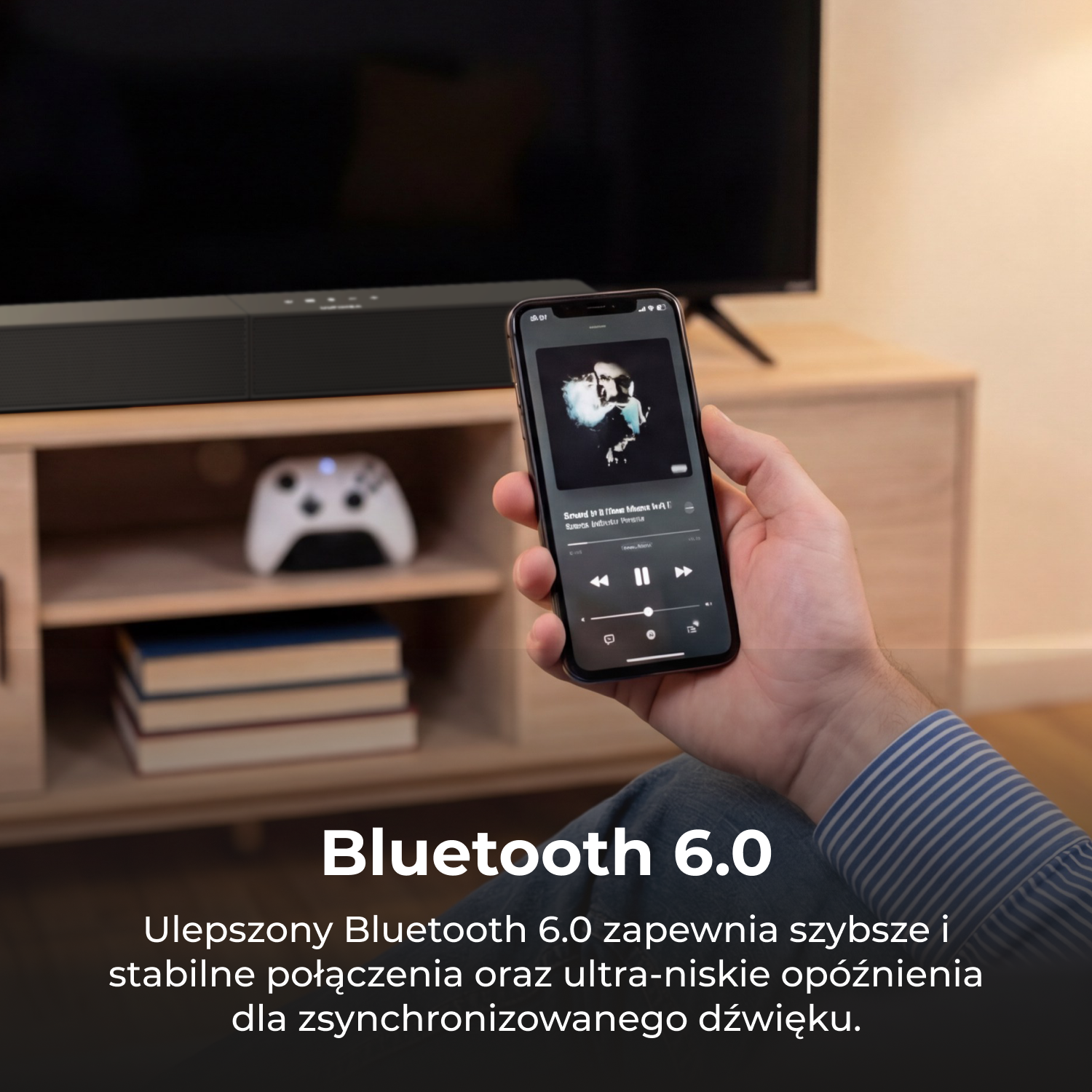 Osoba trzyma smartfon z aplikacją muzyczną. W tle soundbar, telewizor, kontroler.