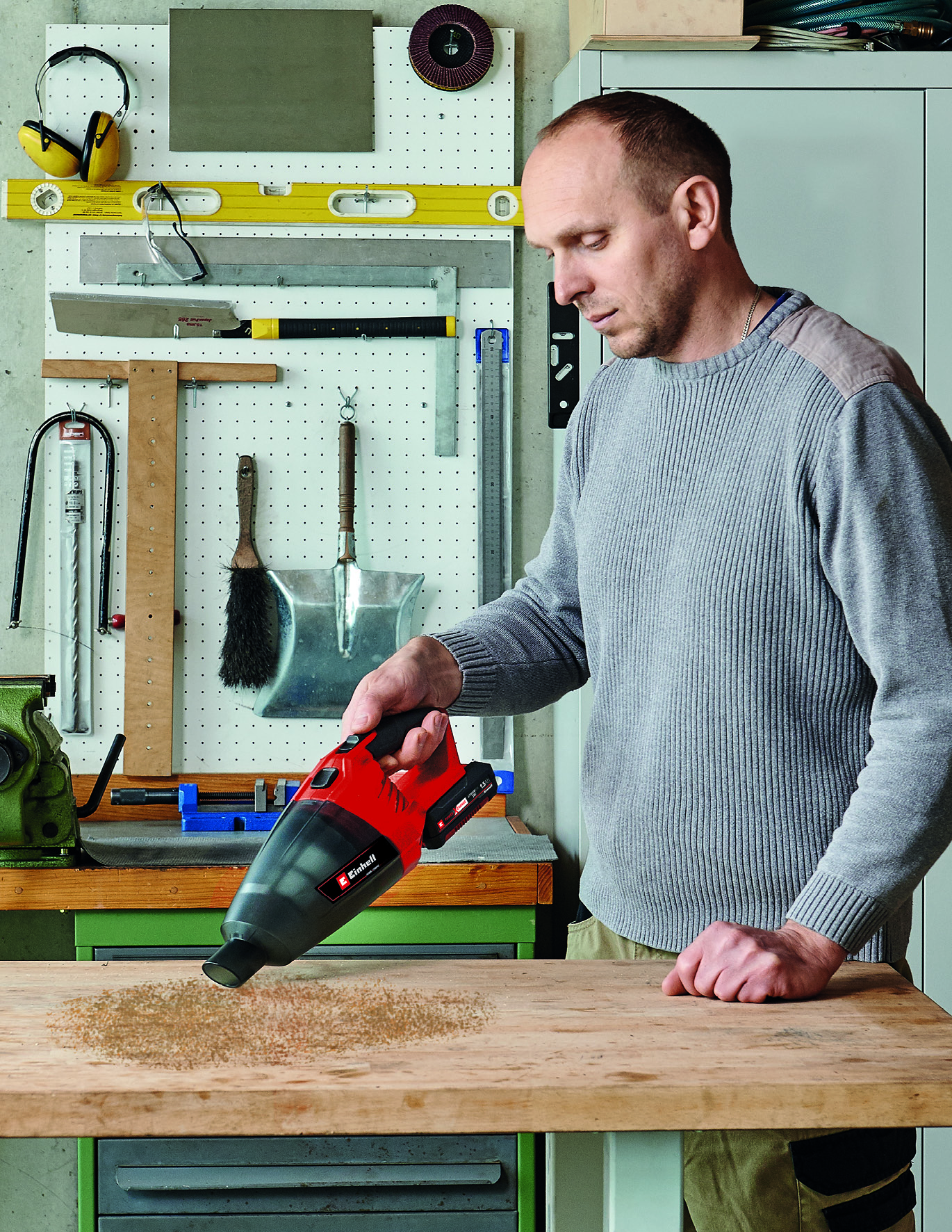 Homme aspirateur copeaux de bois sur établi avec aspirateur rouge.