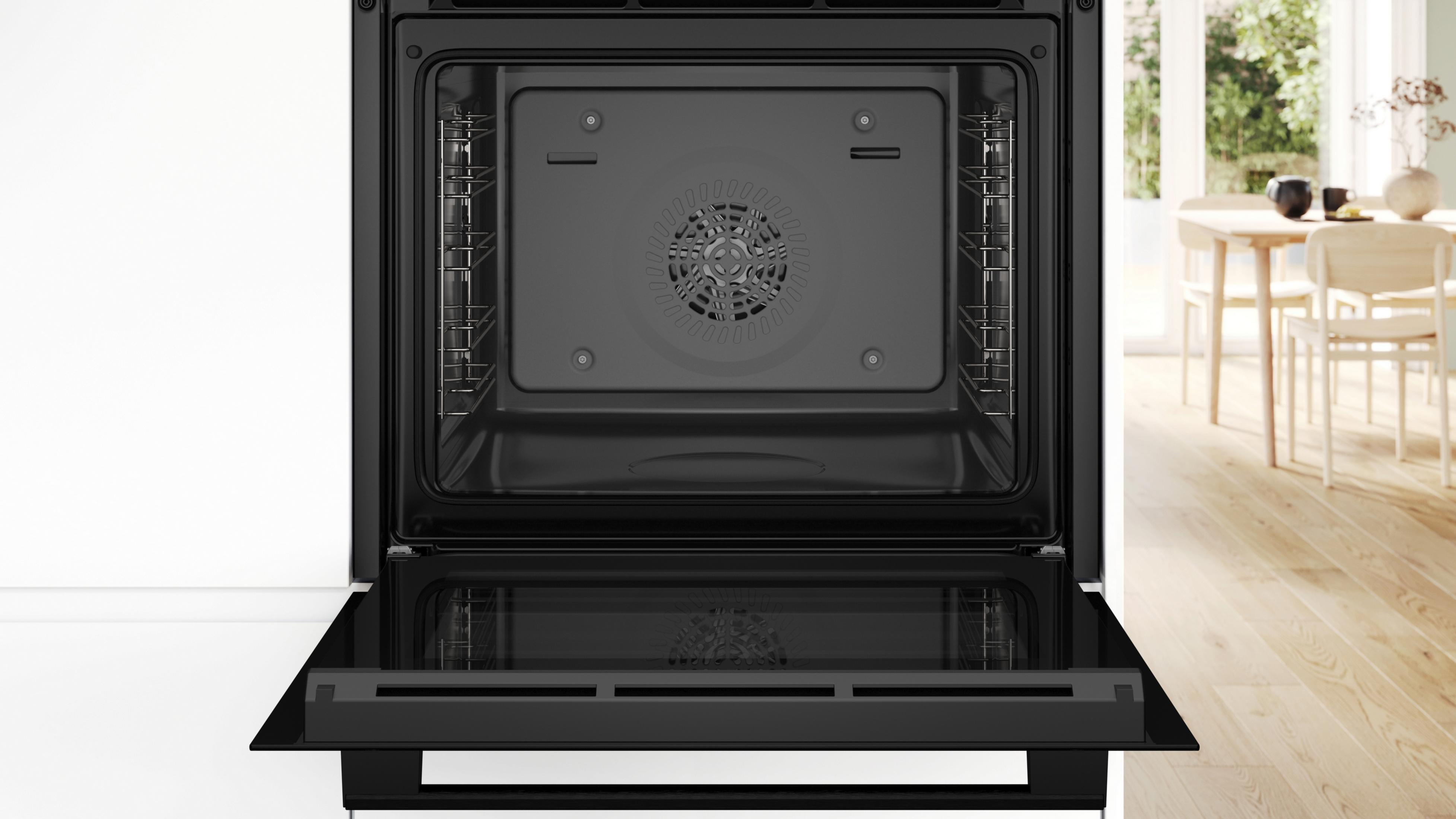 Un four noir ouvert avec grilles et ventilateur argentés. Une table est visible dehors.