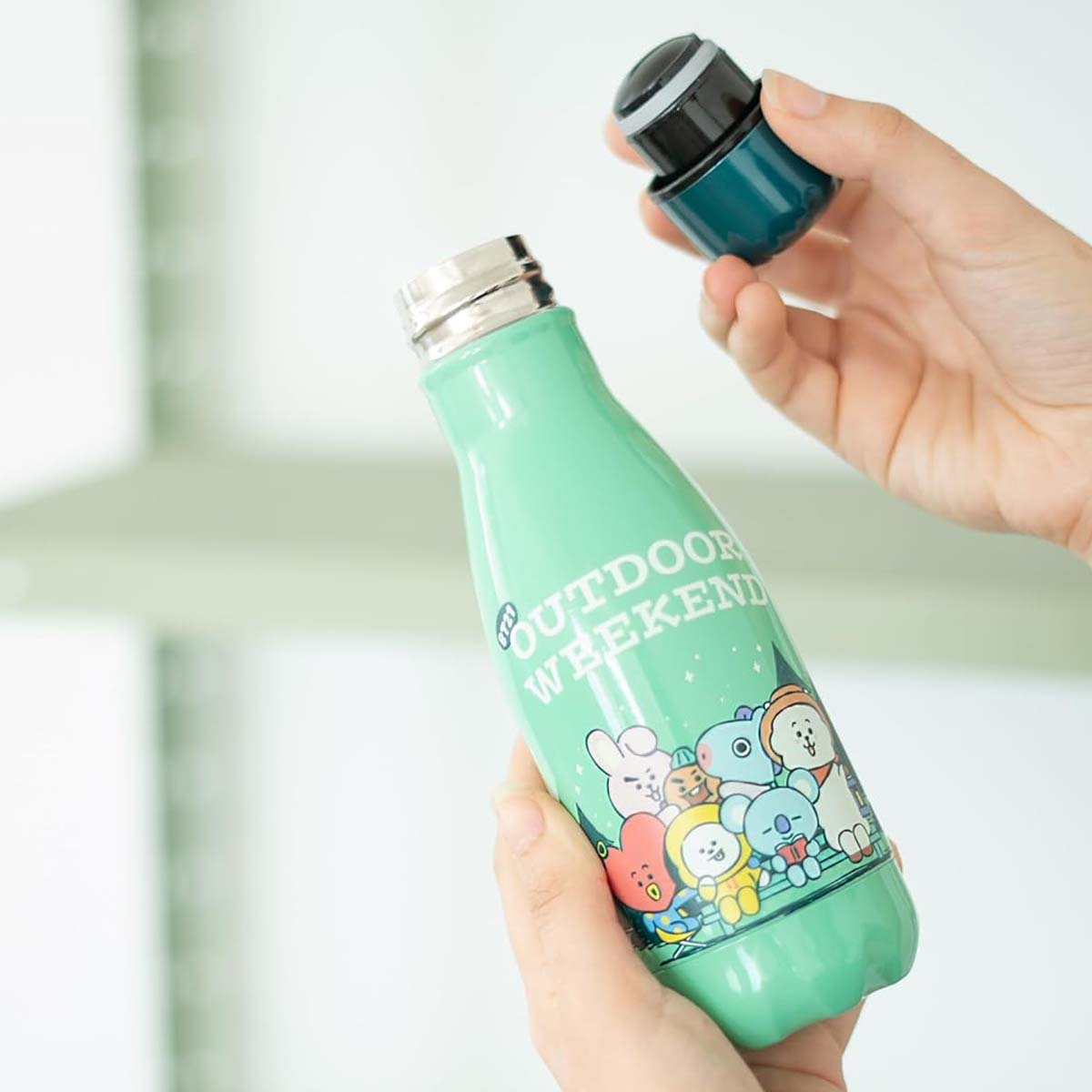 Una borraccia verde chiaro con personaggi dei cartoni animati e la scritta "OUTDOOR WEEKEND".