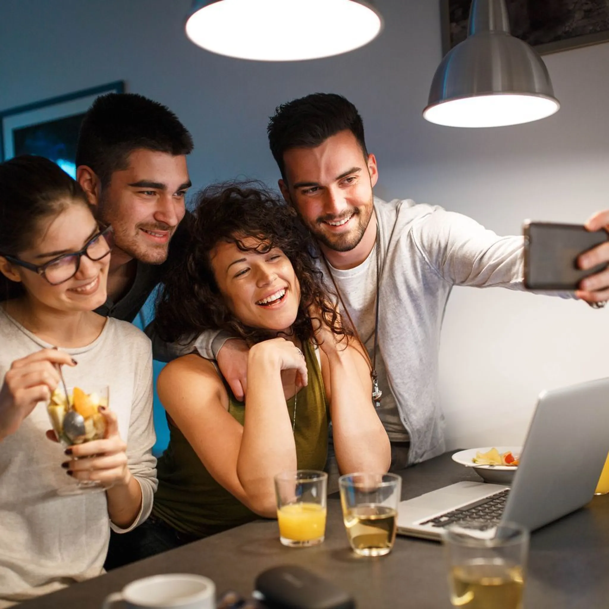 Vier Freunde machen ein Selfie am Tisch mit Getränken und Obst.